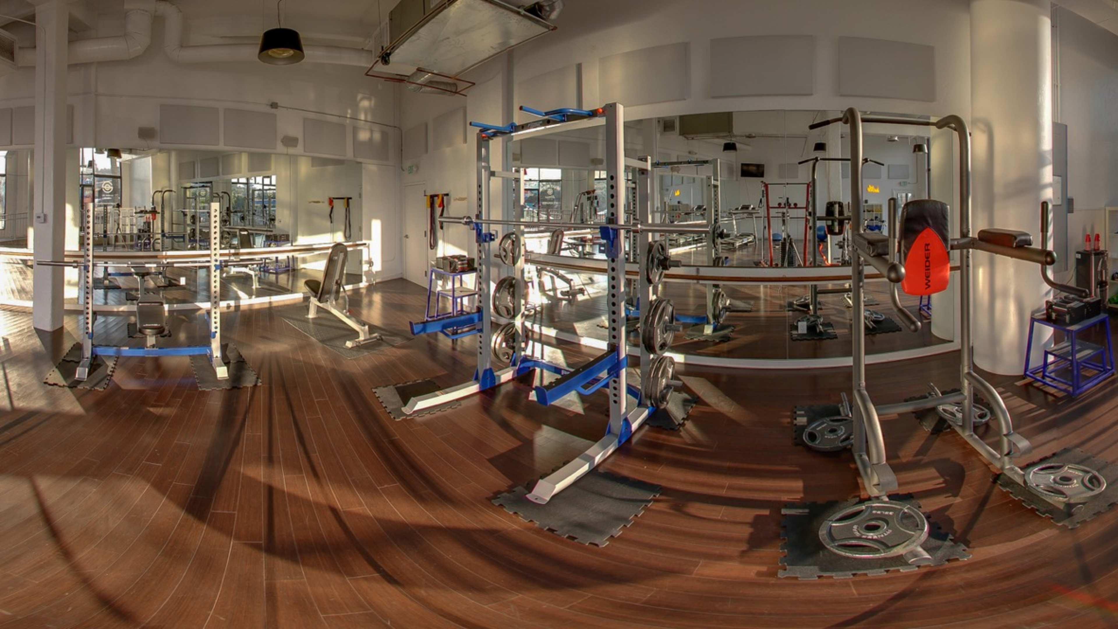 A spacious gym interior with various weightlifting equipment and large mirrors against the walls.