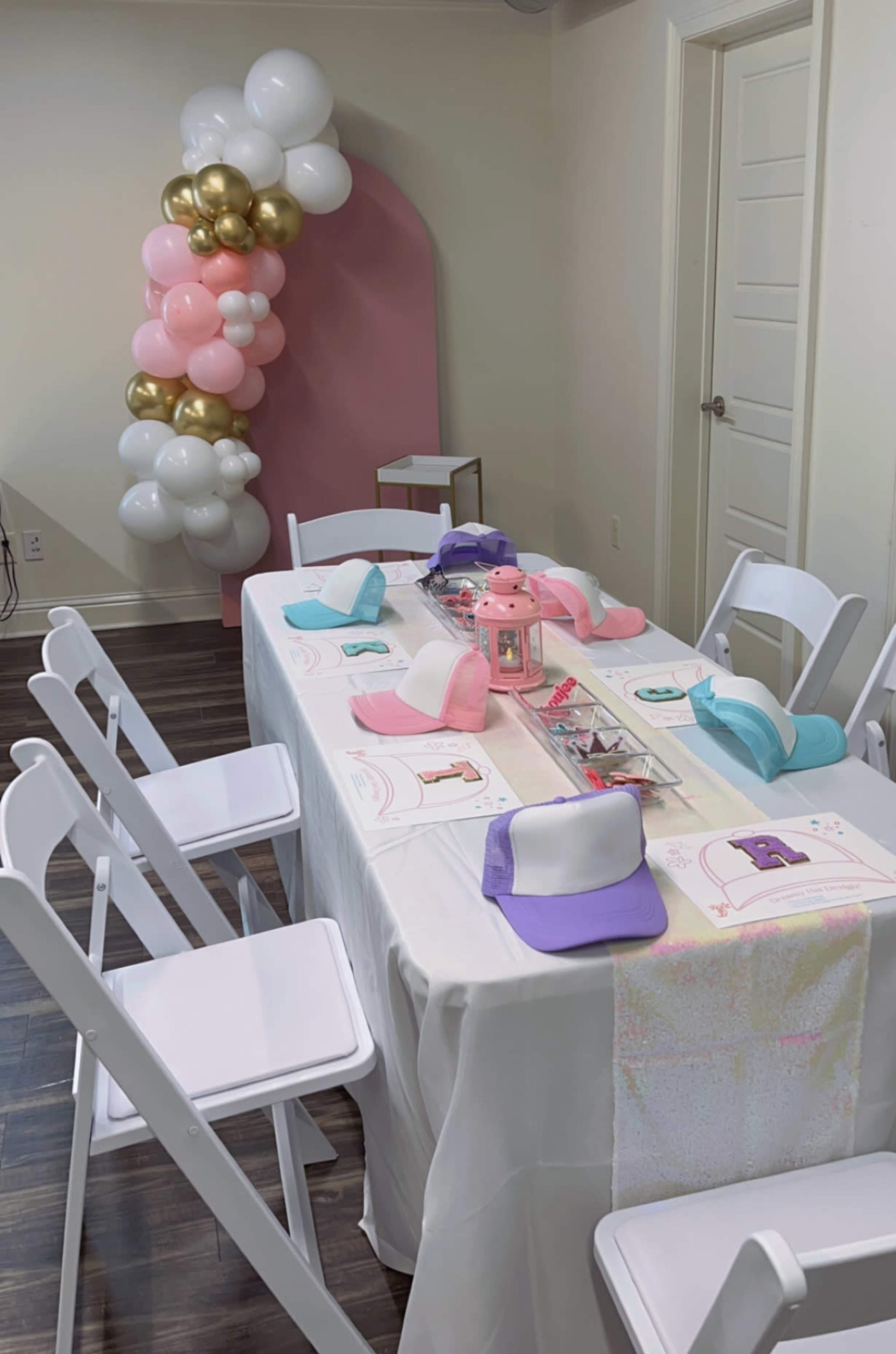 A decorated table with colorful hats and a balloon arch is set up for a celebration in a bright room.