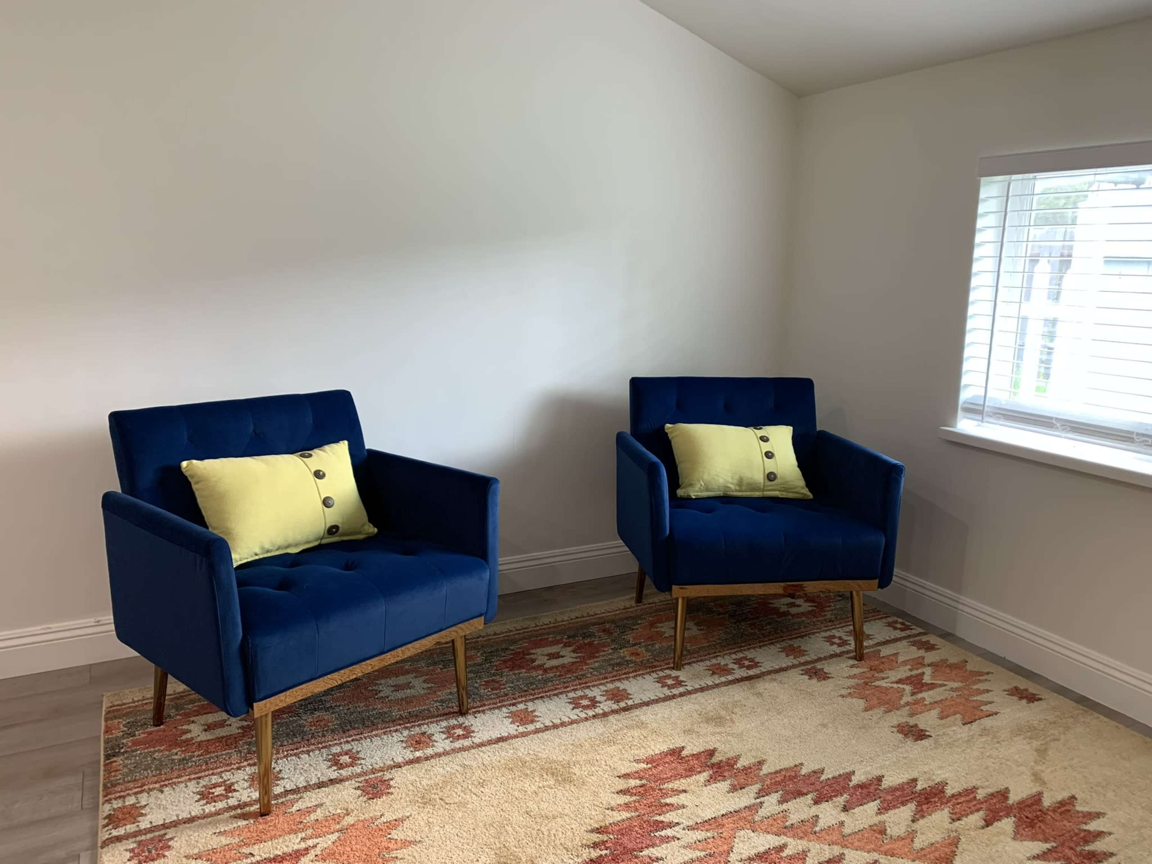 The image shows two blue armchairs with yellow cushions positioned on a patterned rug in a well-lit room with a window.