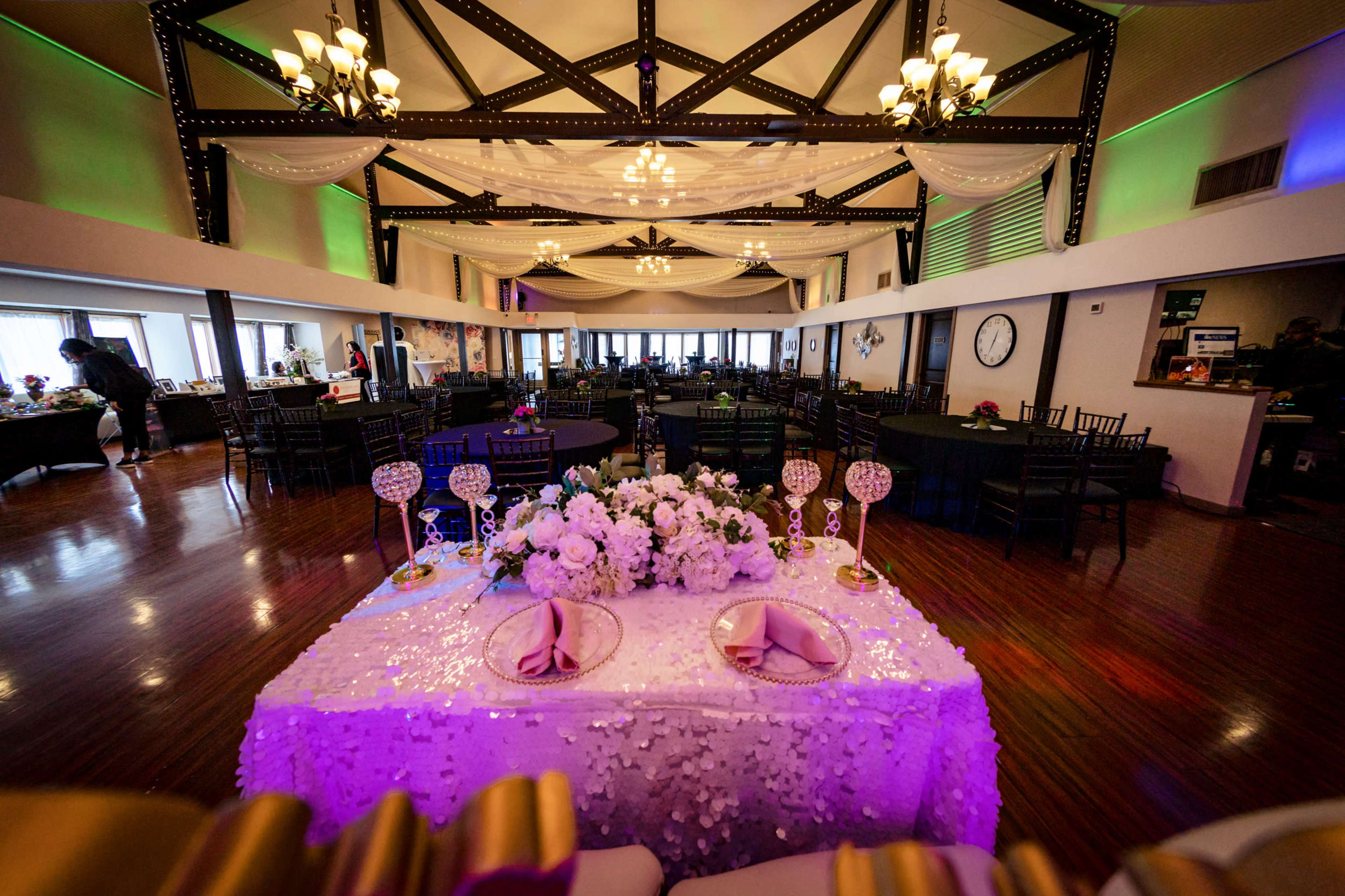 A spacious banquet hall with tables set for a wedding reception, featuring a decorated head table adorned with floral arrangements and elegant centerpieces.