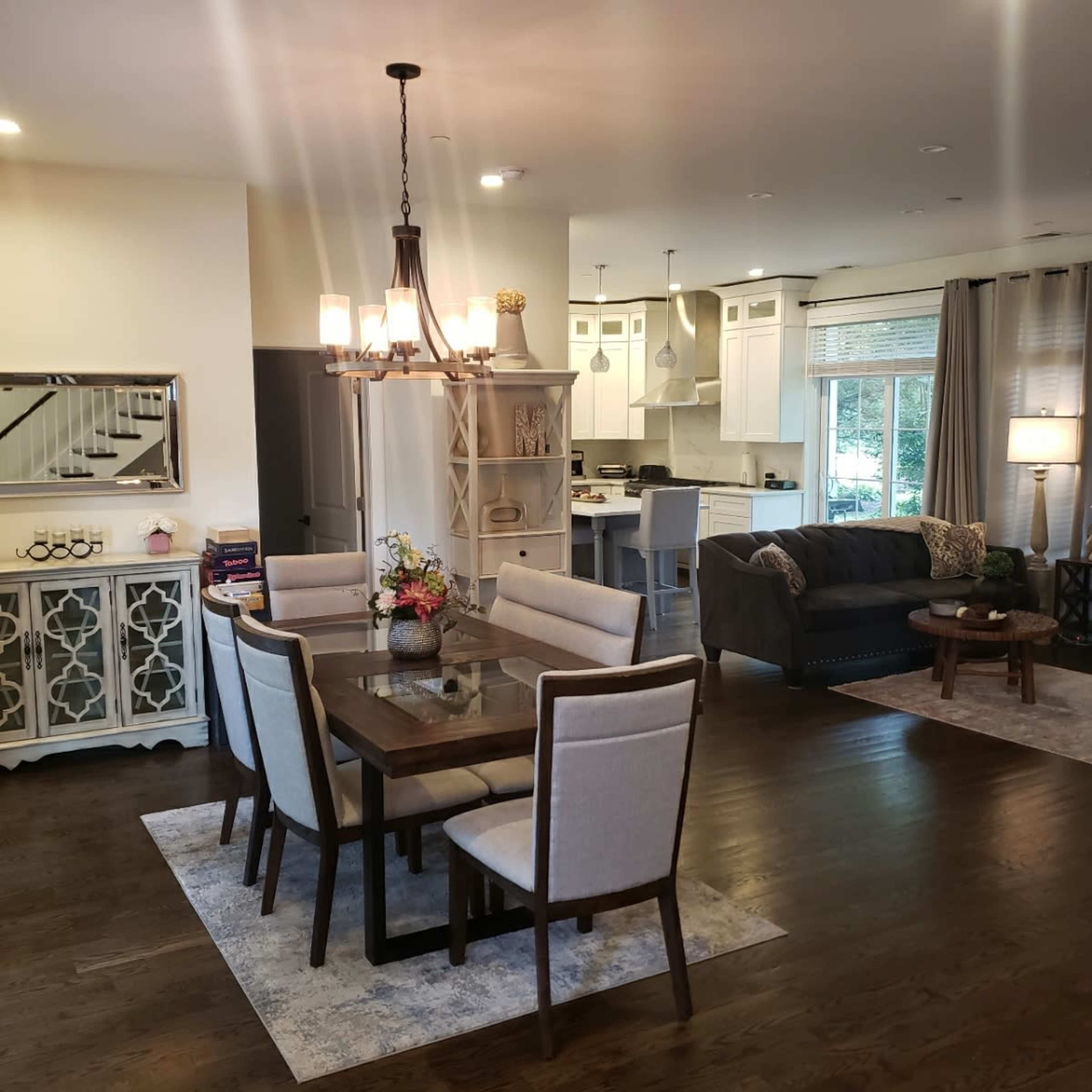 A dining area with a wooden table and chairs adjacent to a modern kitchen and living room, featuring a couch and a lamp.