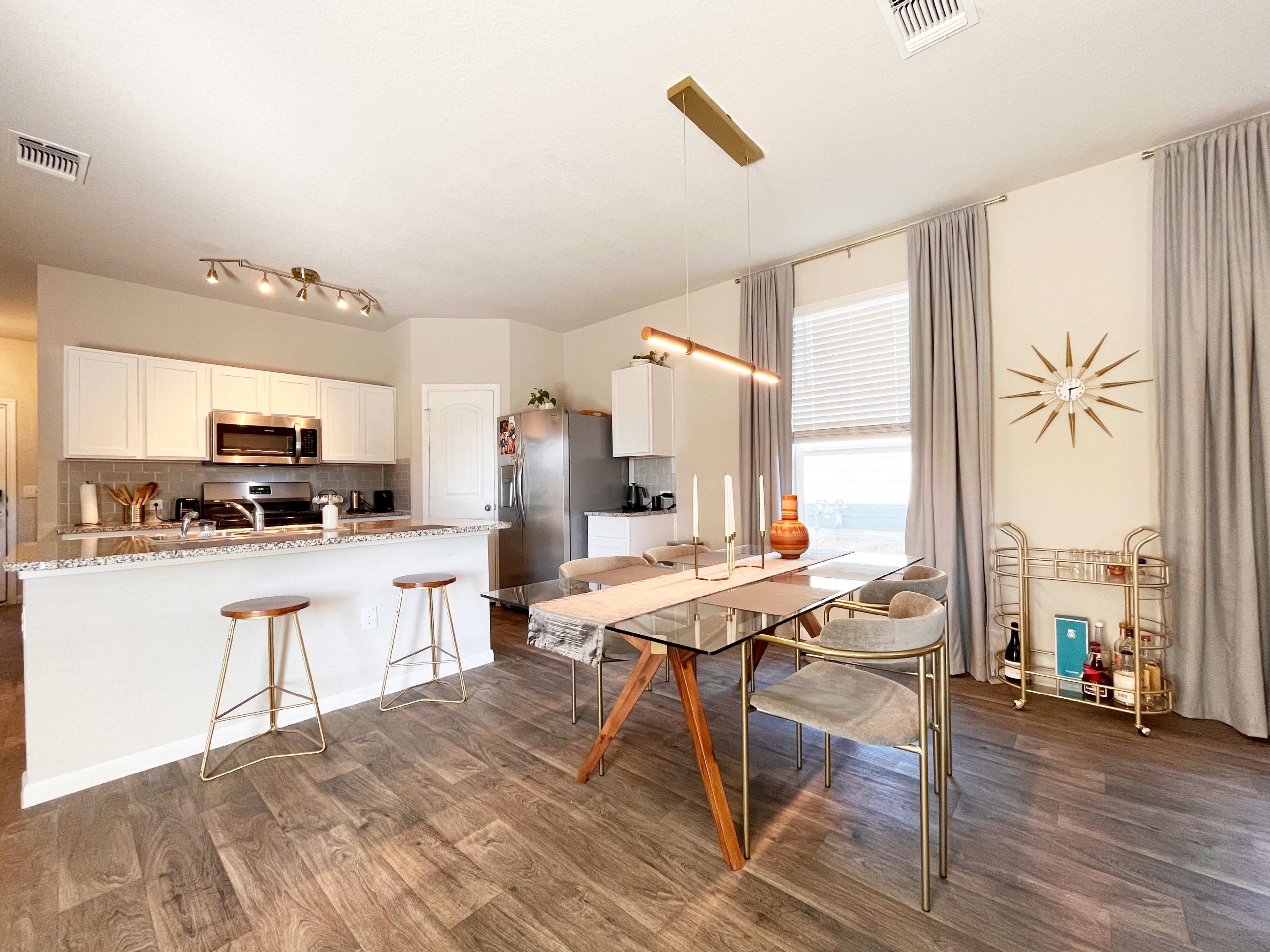 A modern kitchen and dining area features a large table with stylish chairs, a kitchen island with bar stools, and stainless steel appliances.
