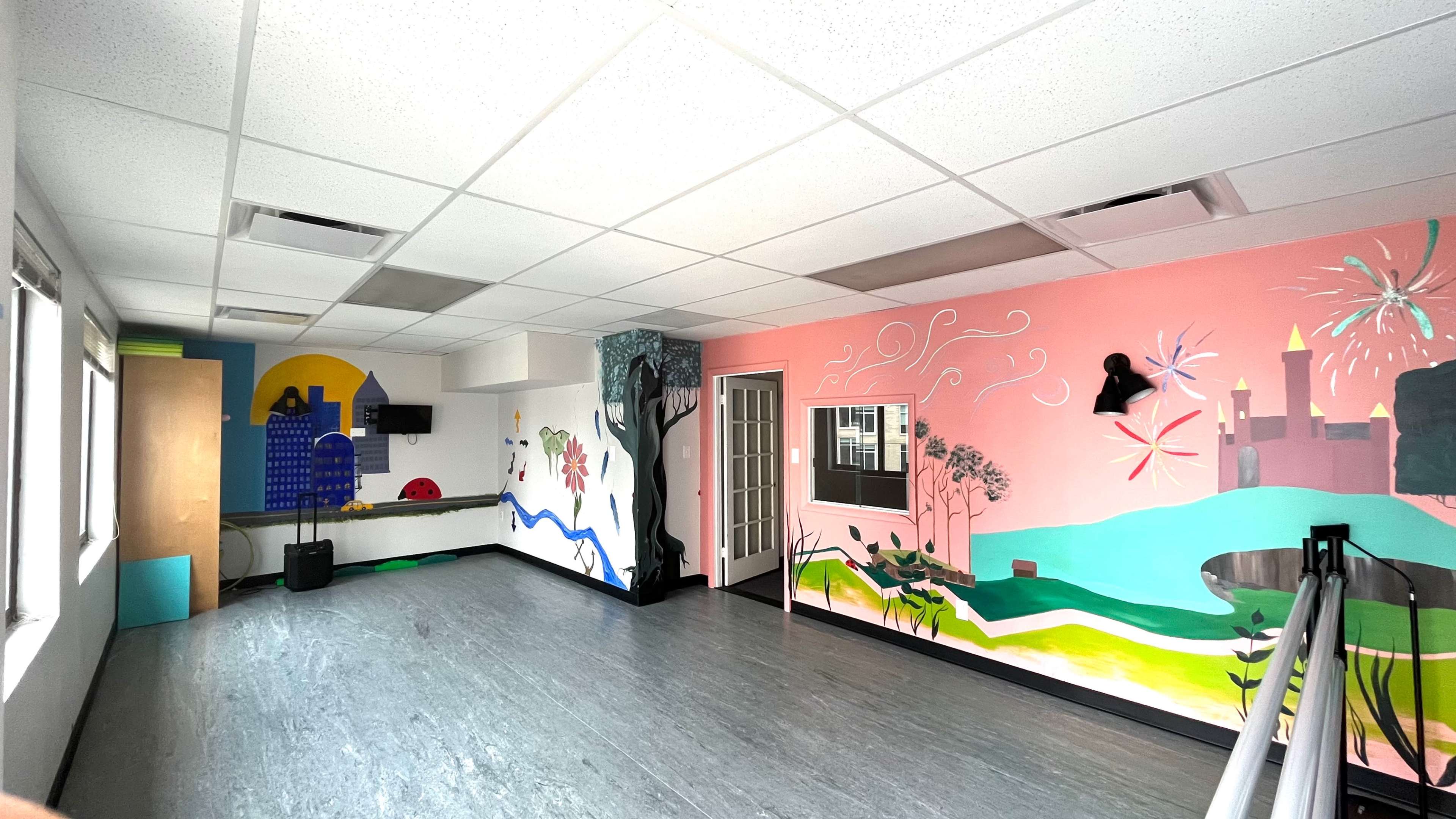 The room features colorful murals on the walls, a large open space with gray flooring, and windows allowing natural light.
