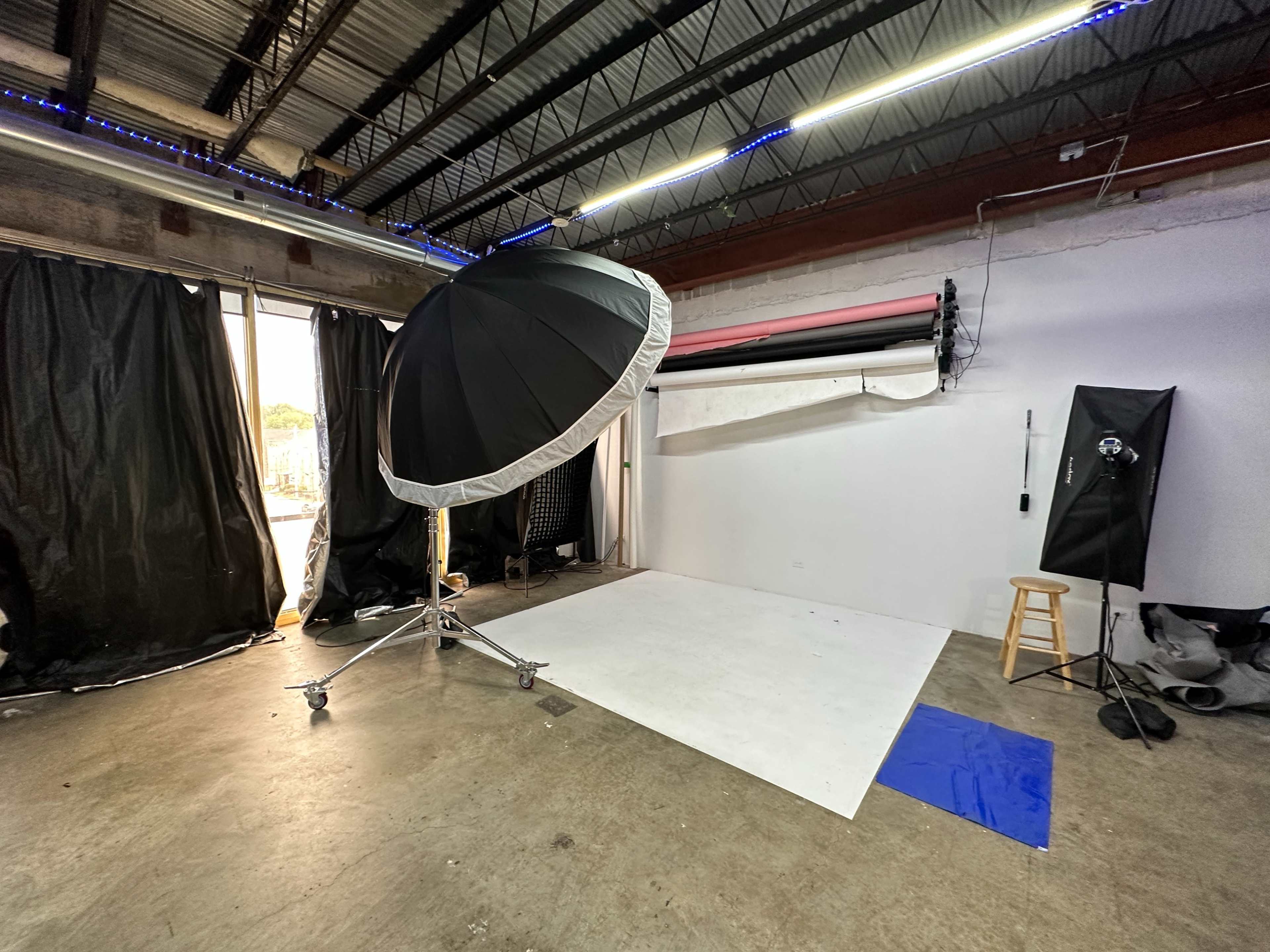 A photography studio featuring a large softbox, a backdrop setup, and various equipment along a concrete floor.