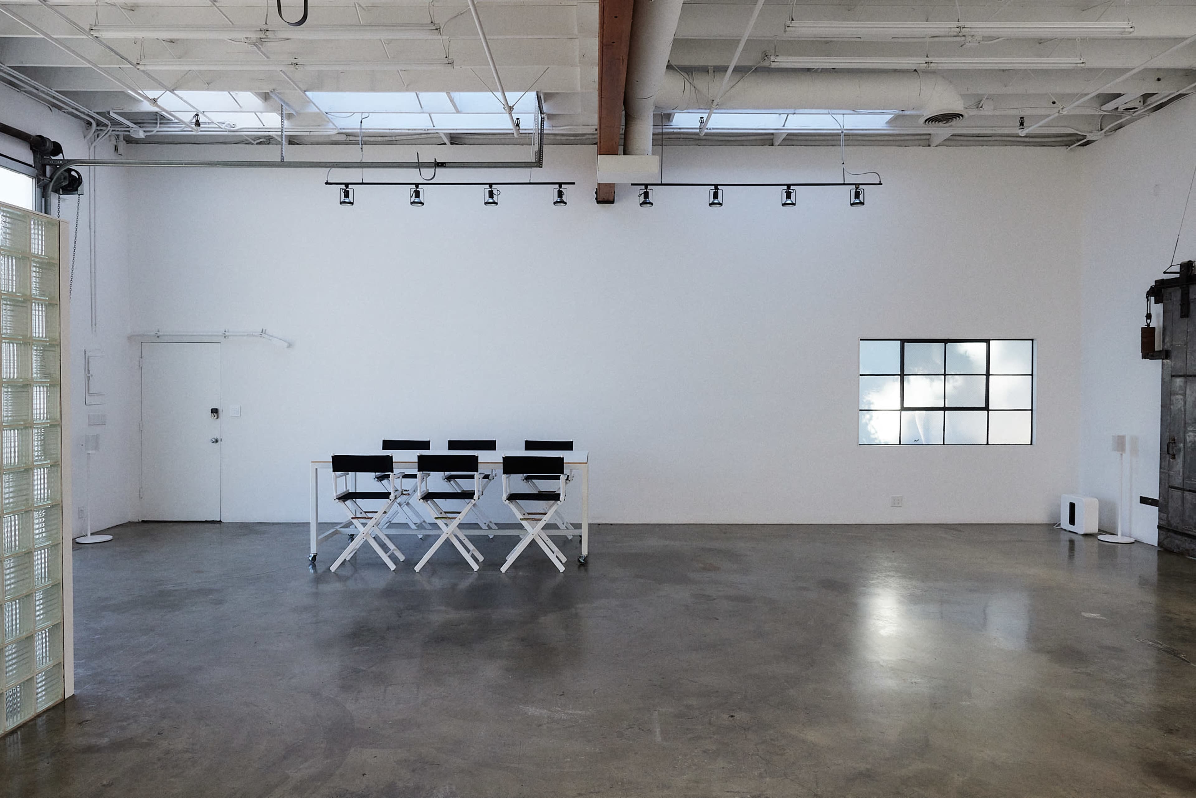 An empty room with a polished concrete floor, a row of four black director's chairs, and a large window with multiple panes.