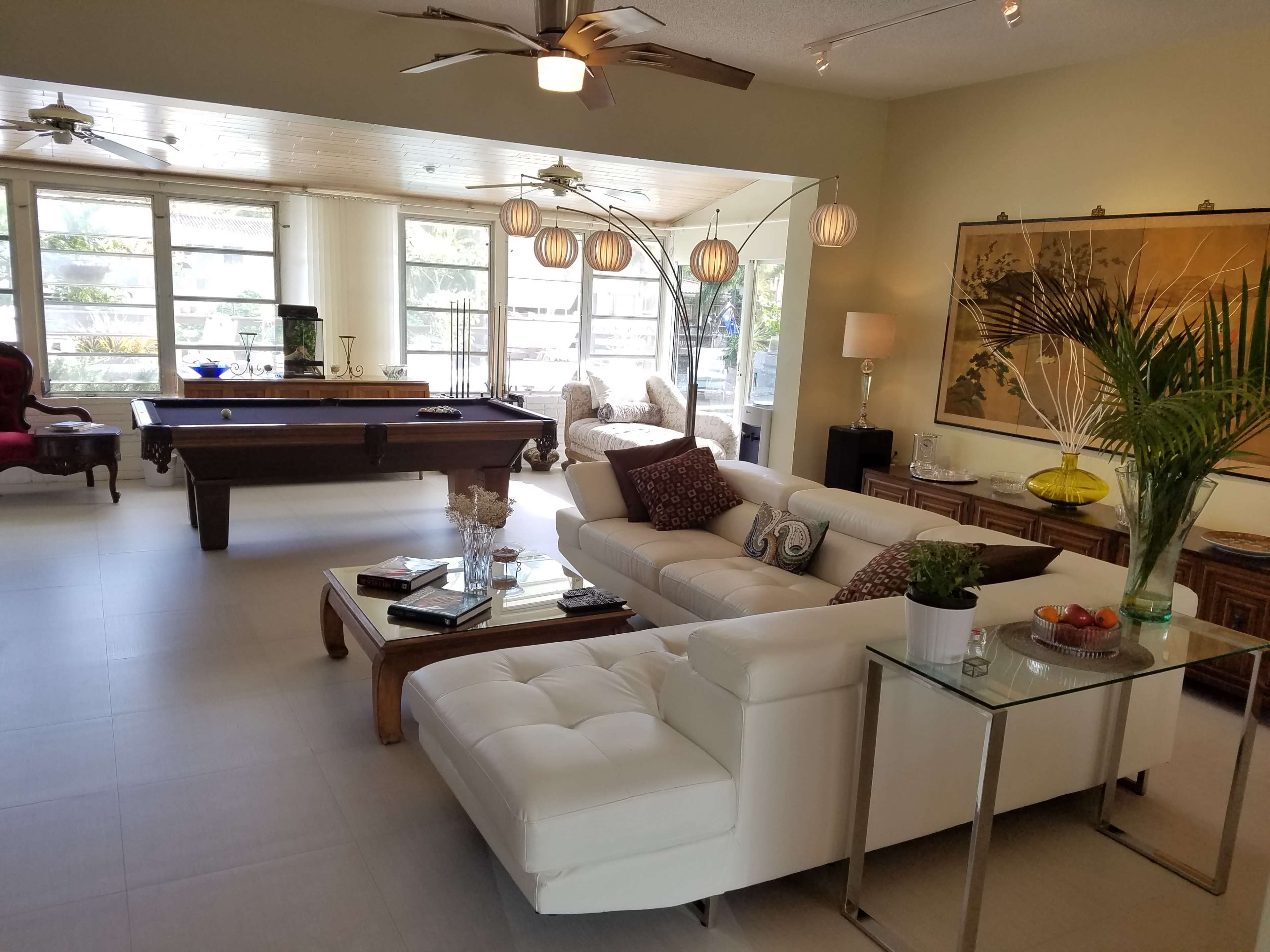 A spacious living room with a white sectional sofa, a pool table, and large windows that provide ample natural light.