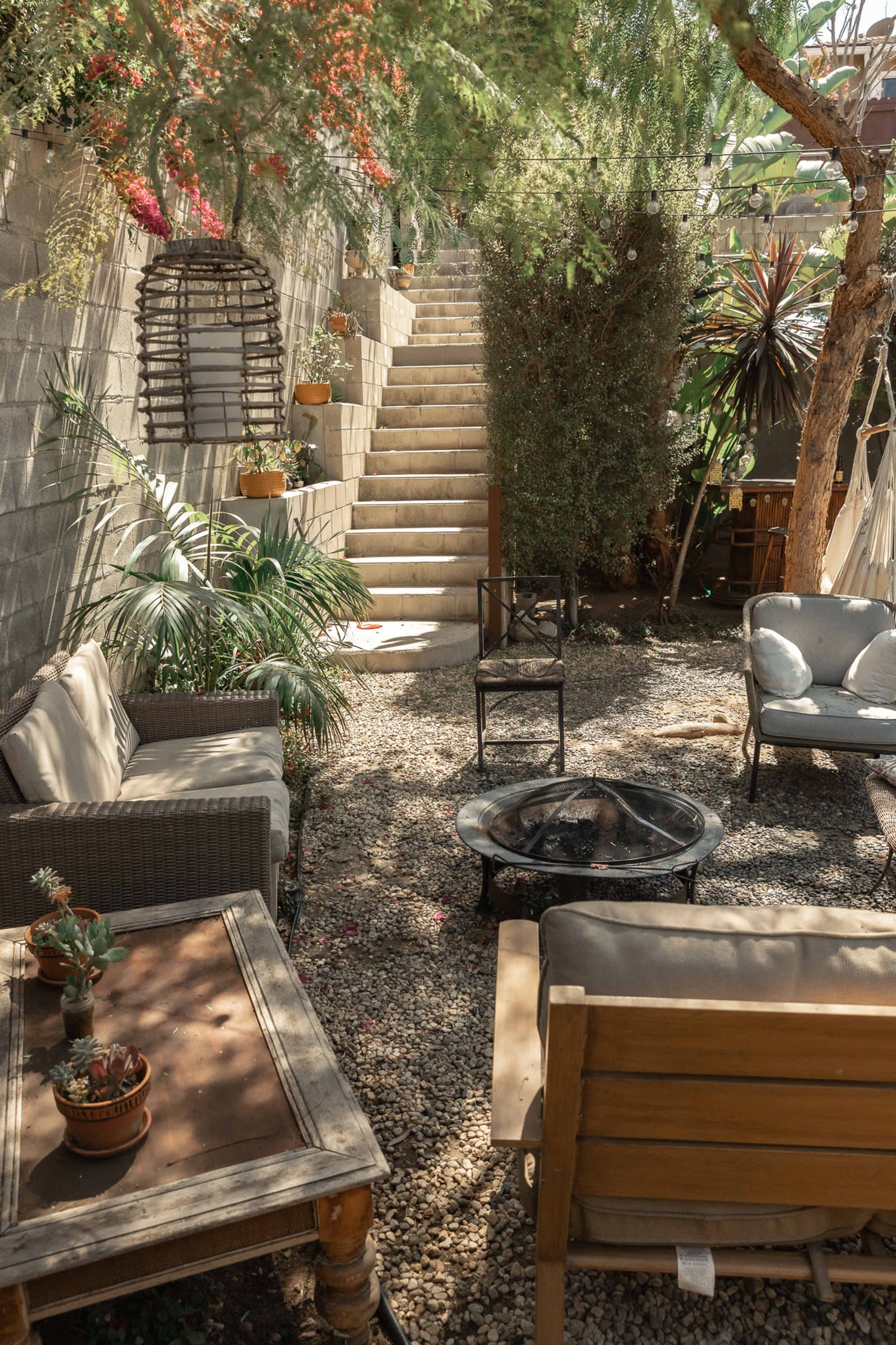 A landscaped garden area with a stone pathway leading up to stairs, surrounded by various plants and outdoor seating arrangements.