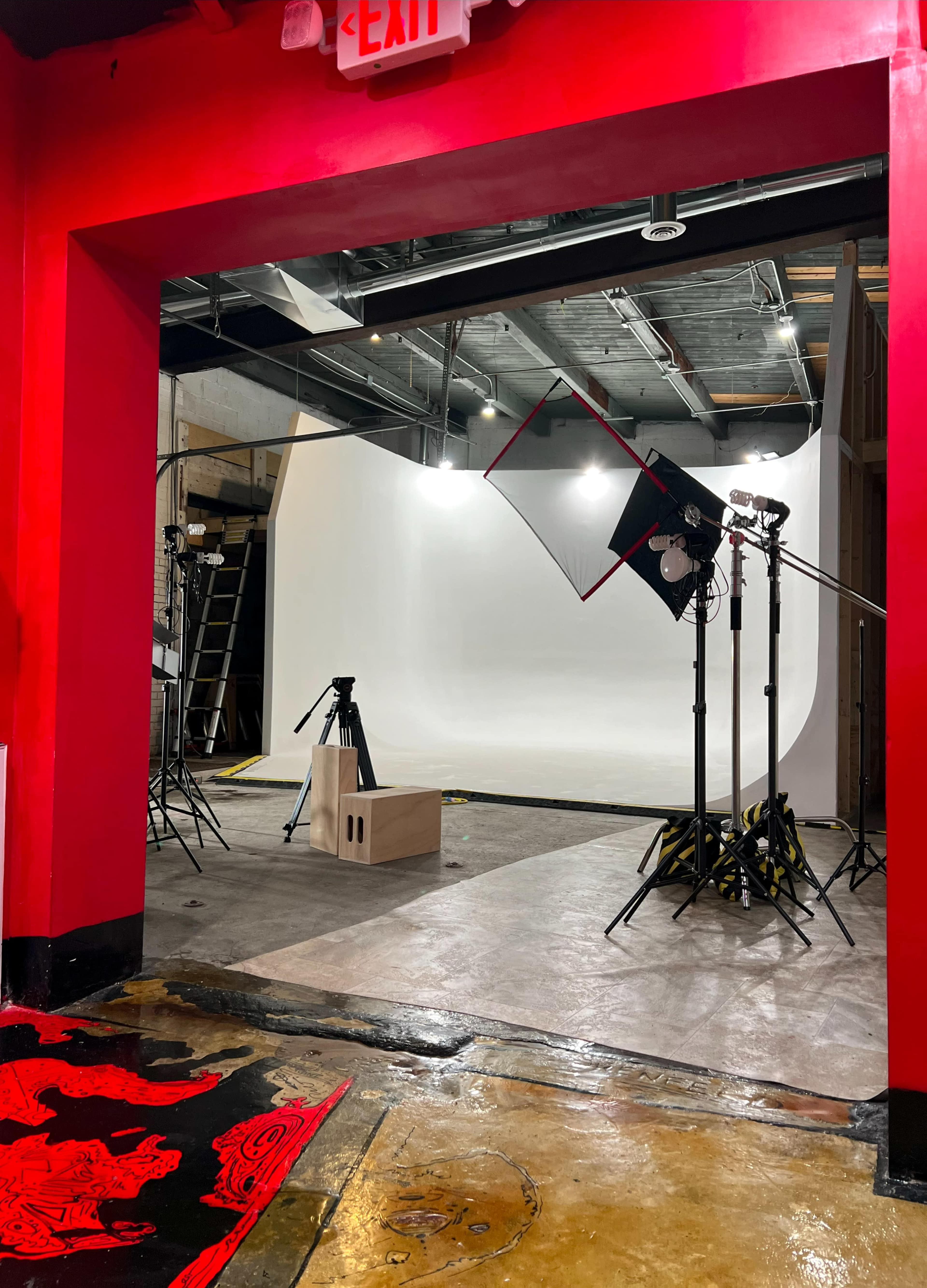 A photography studio is visible through an open doorway, featuring a white backdrop, lighting equipment, and a wooden platform.