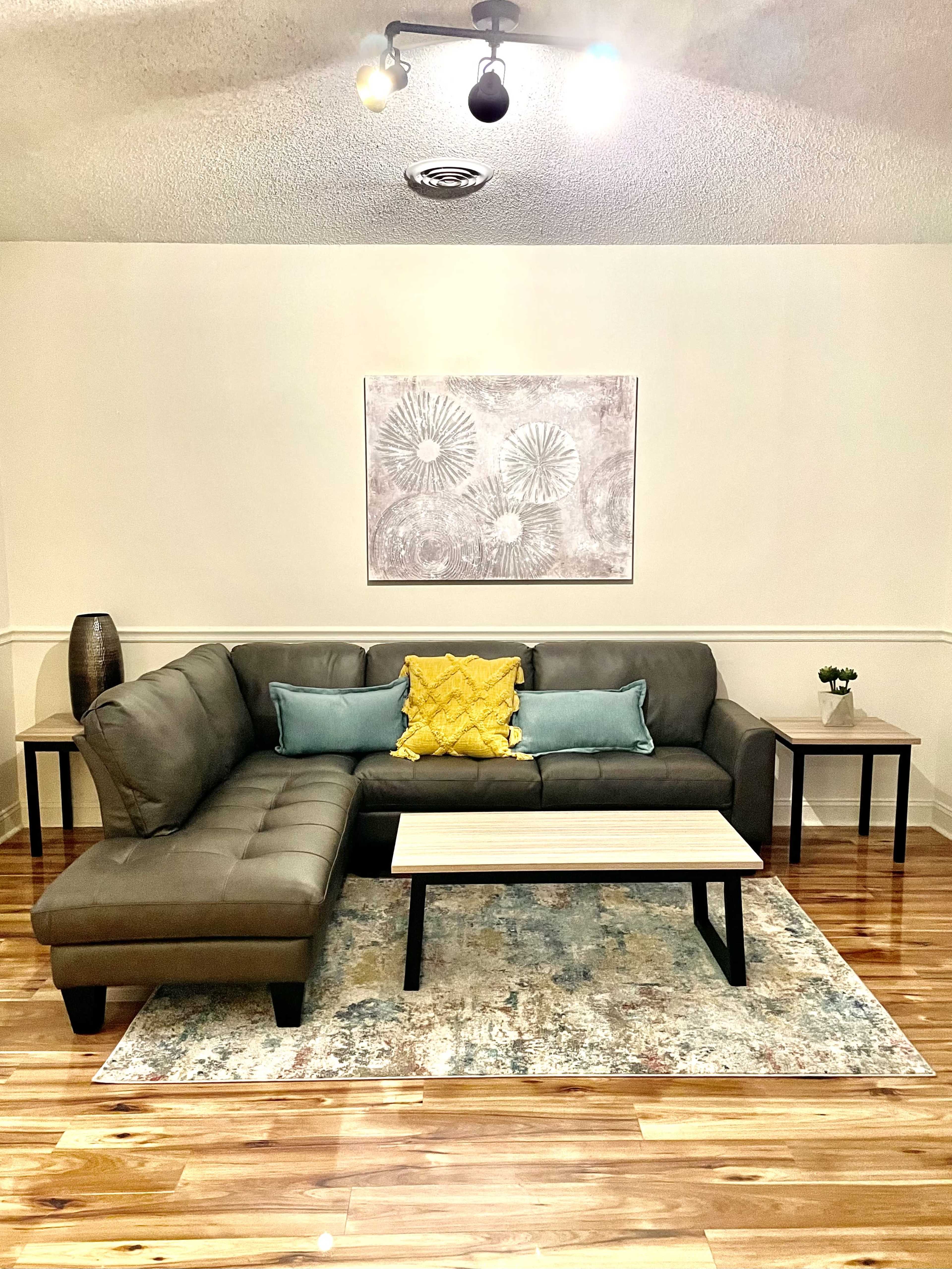 A modern living room with a grey sectional sofa, a coffee table, and decorative pillows on a patterned area rug.
