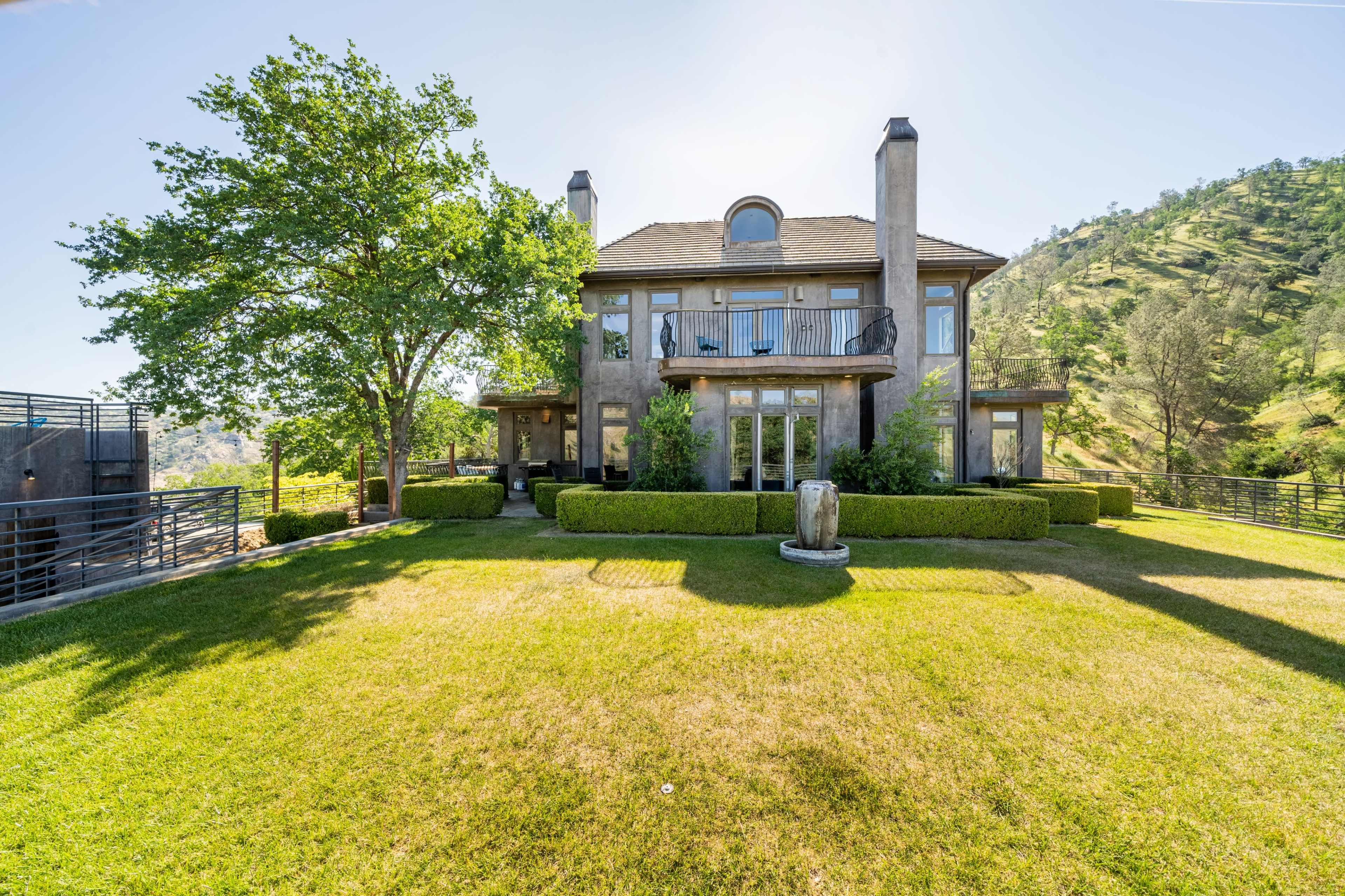 A large two-story house with a front lawn, surrounded by trees and hills in the background.