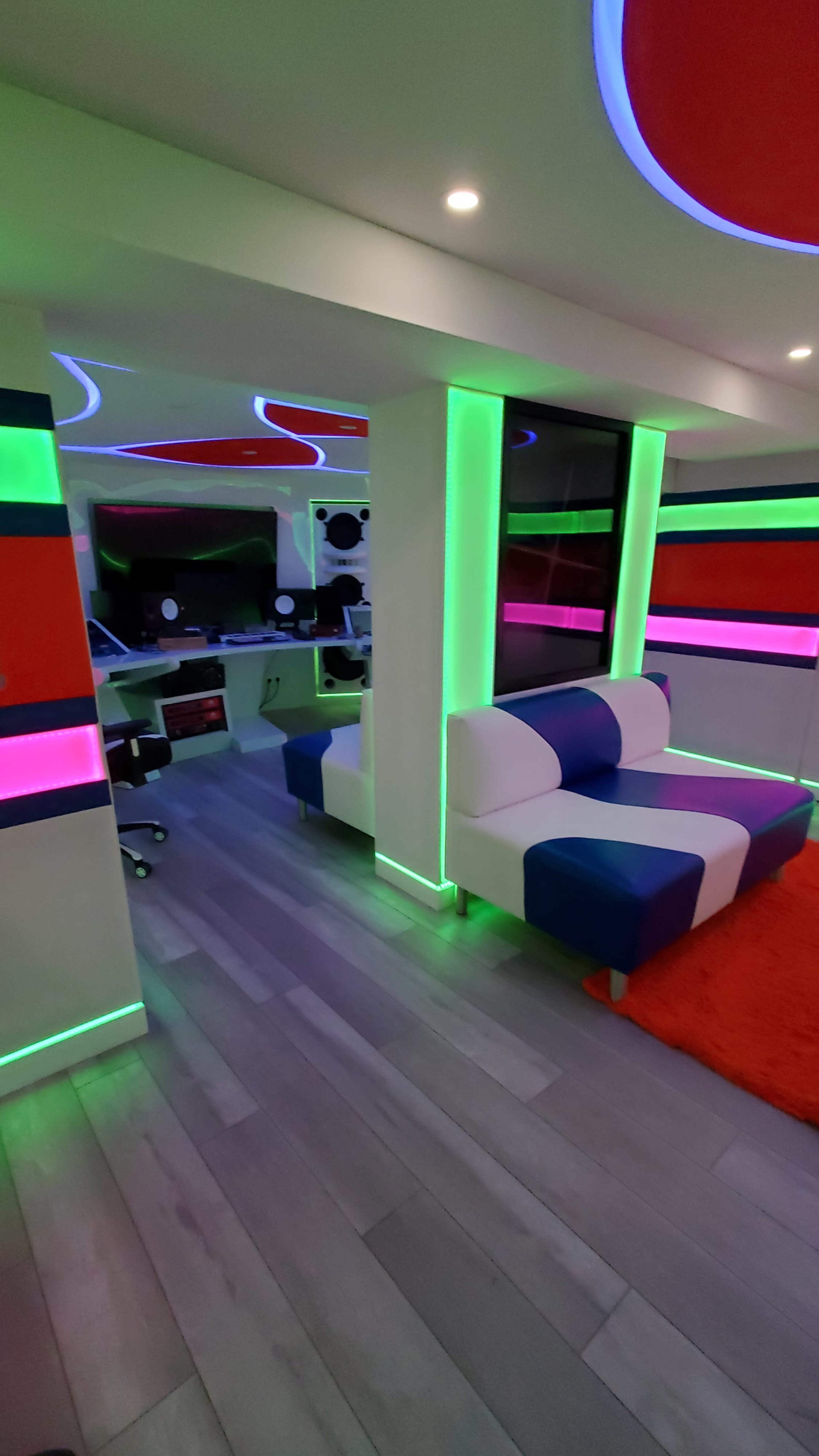 A modern room features colorful LED lighting, a sleek white sofa, and a workstation with computers.