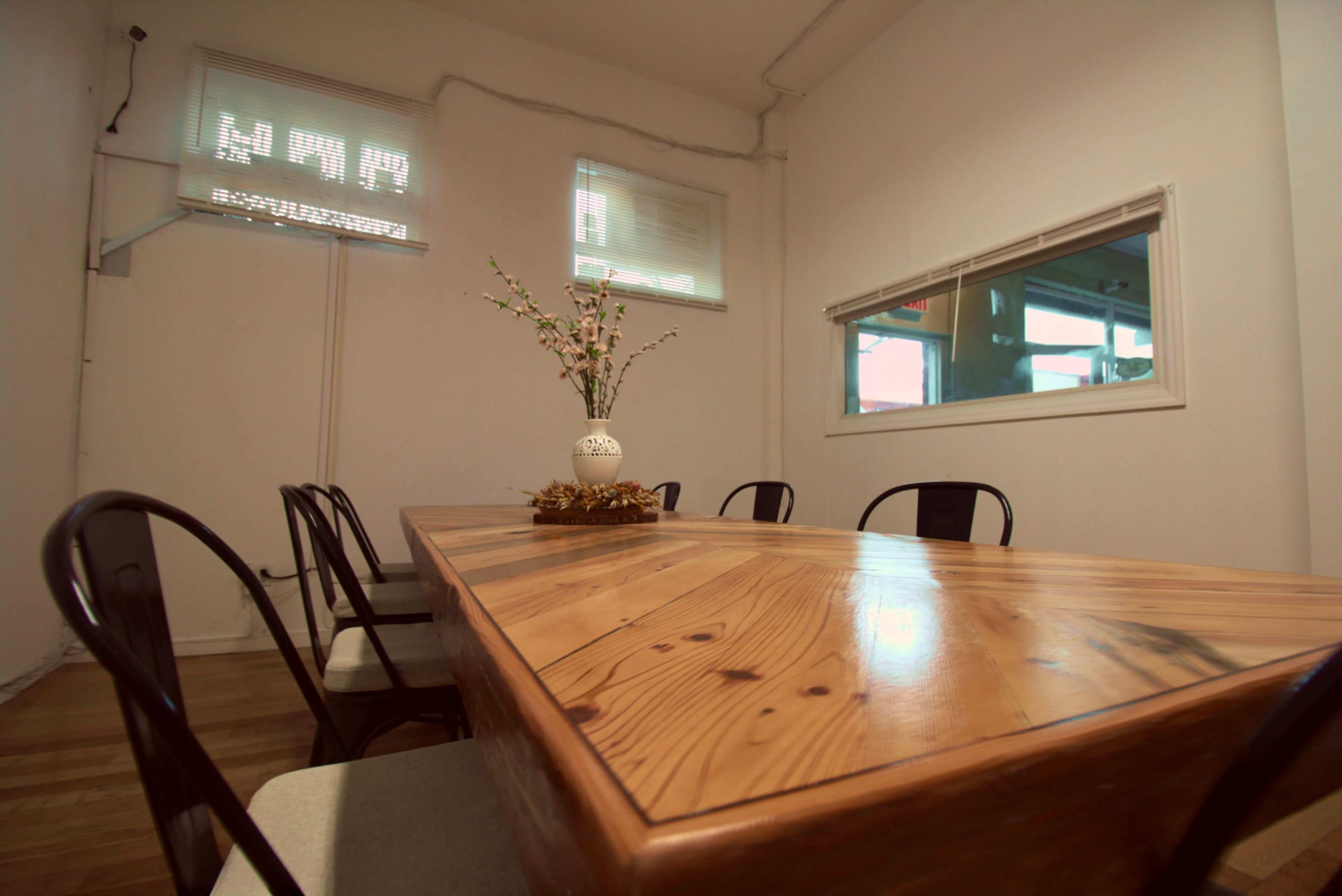 A long wooden table with a floral centerpiece is surrounded by black chairs in a well-lit room.