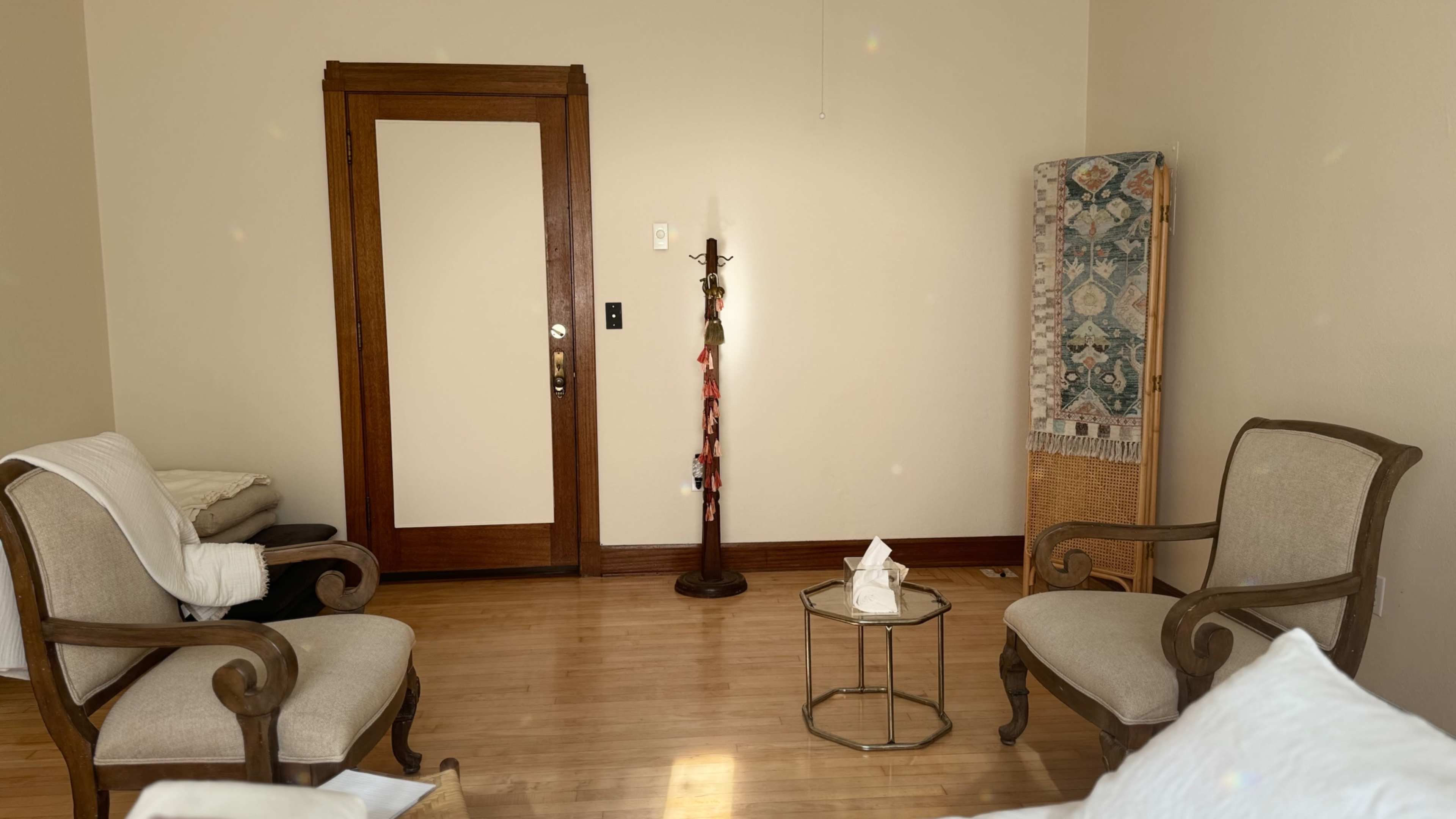 A light-colored room features two armchairs, a small table, a standing lamp, and a decorative screen near the door.