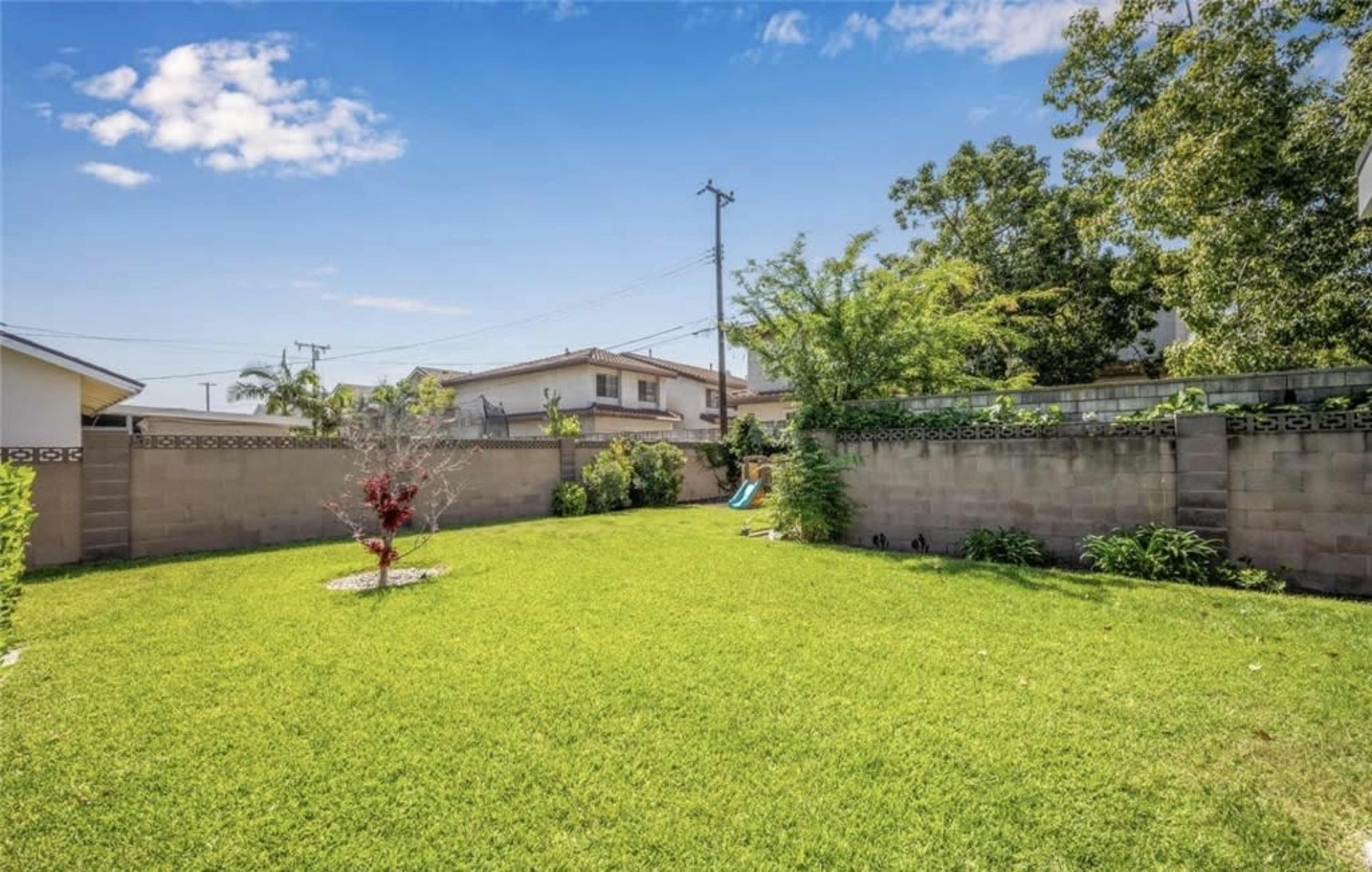 The image shows a grassy backyard enclosed by stone walls, featuring a small tree and a slide in the corner.