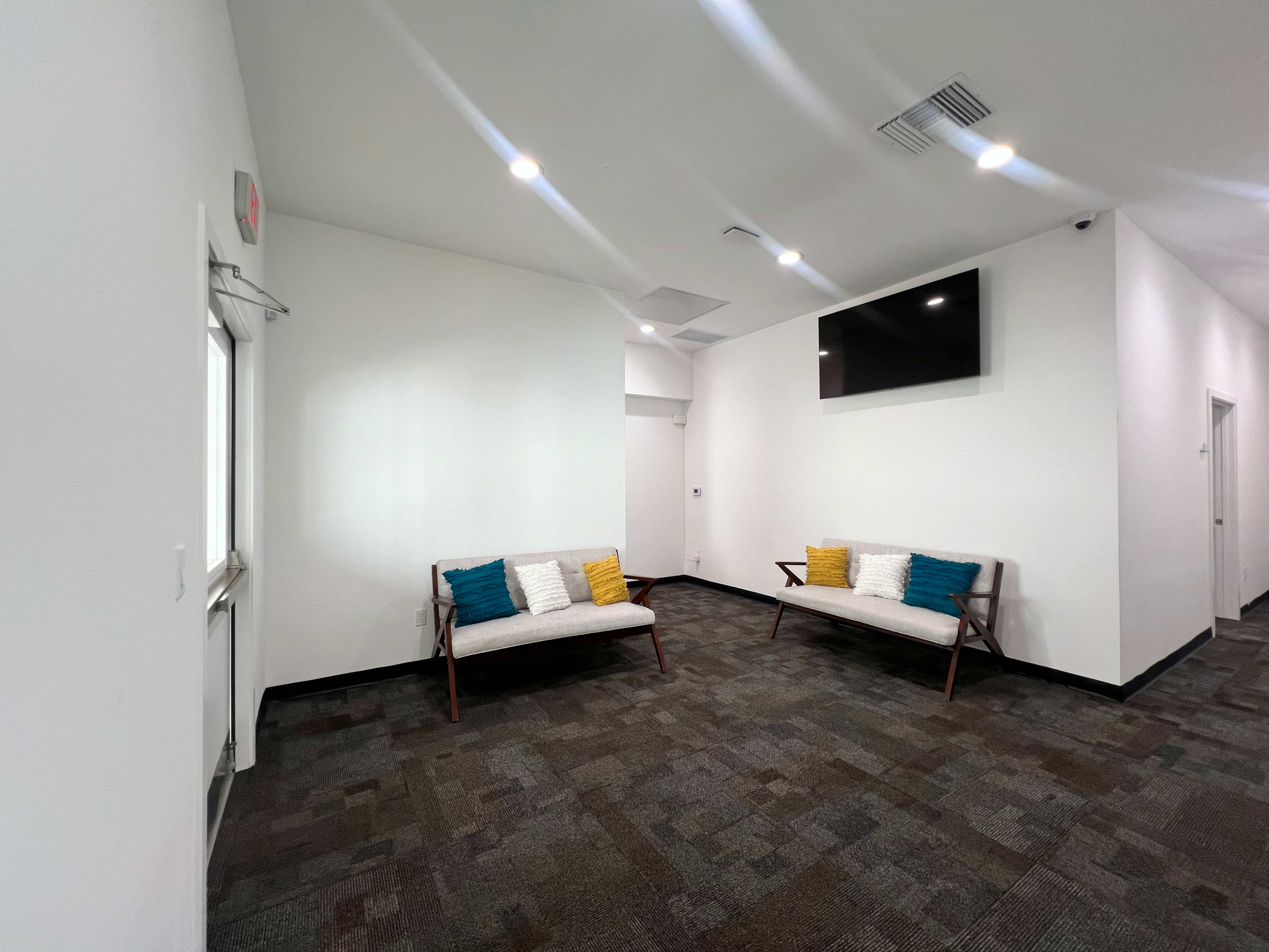 A modern waiting area featuring two benches with cushions, a wall-mounted television, and neutral-colored walls.