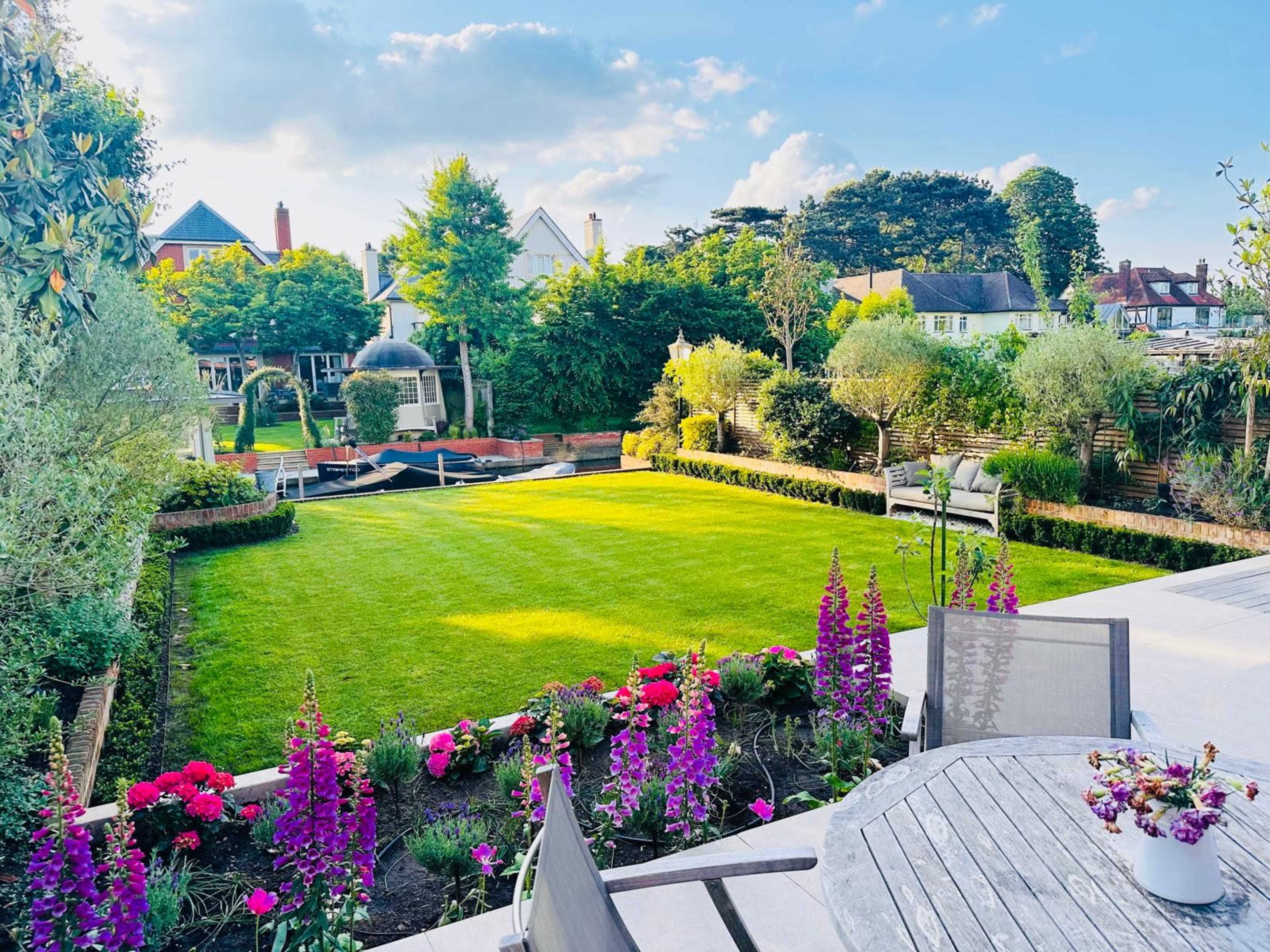 The image shows a well-maintained garden featuring a large green lawn surrounded by colorful flower beds and a seating area.