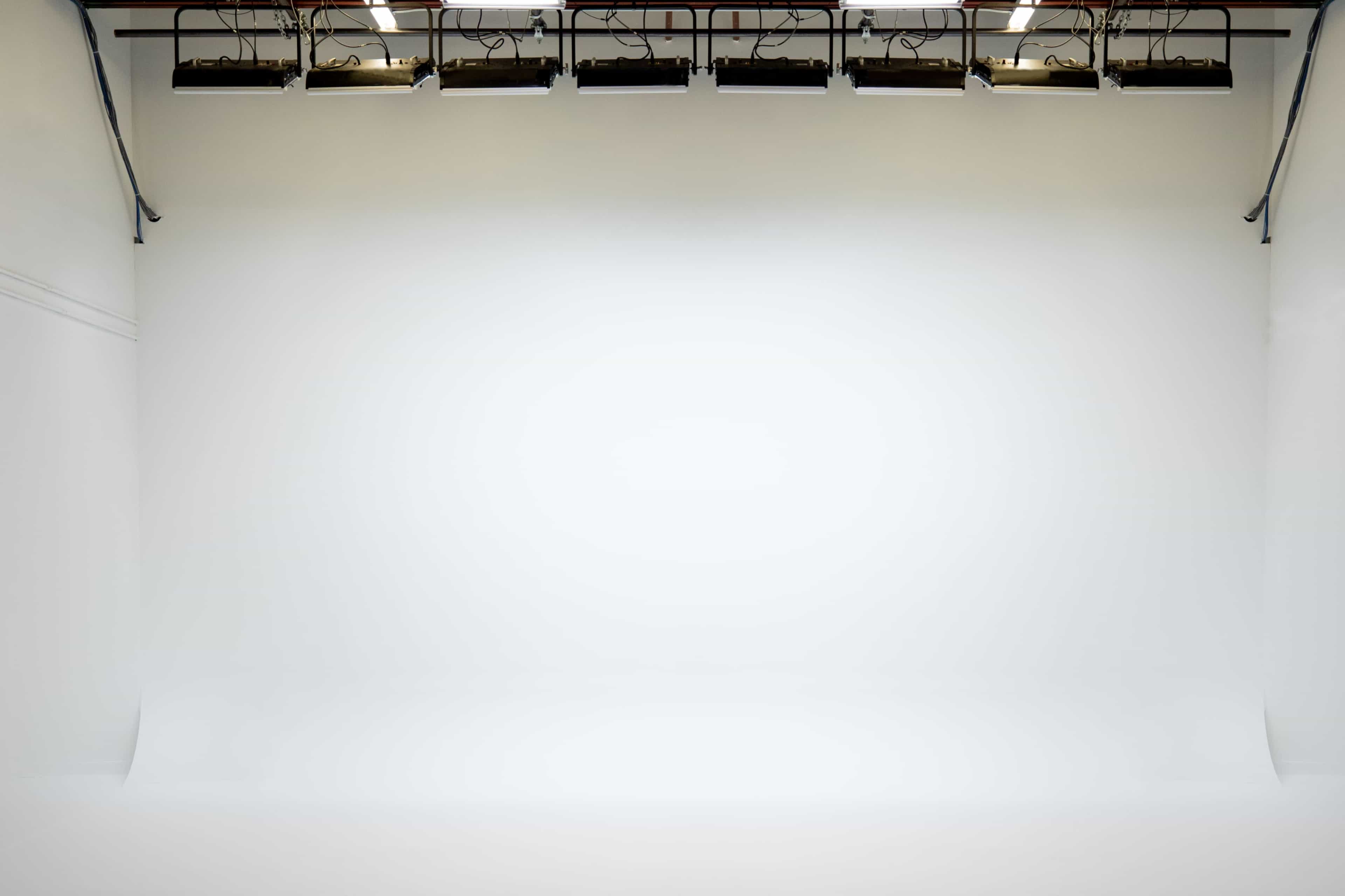 An empty photography studio with white walls and a seamless backdrop.