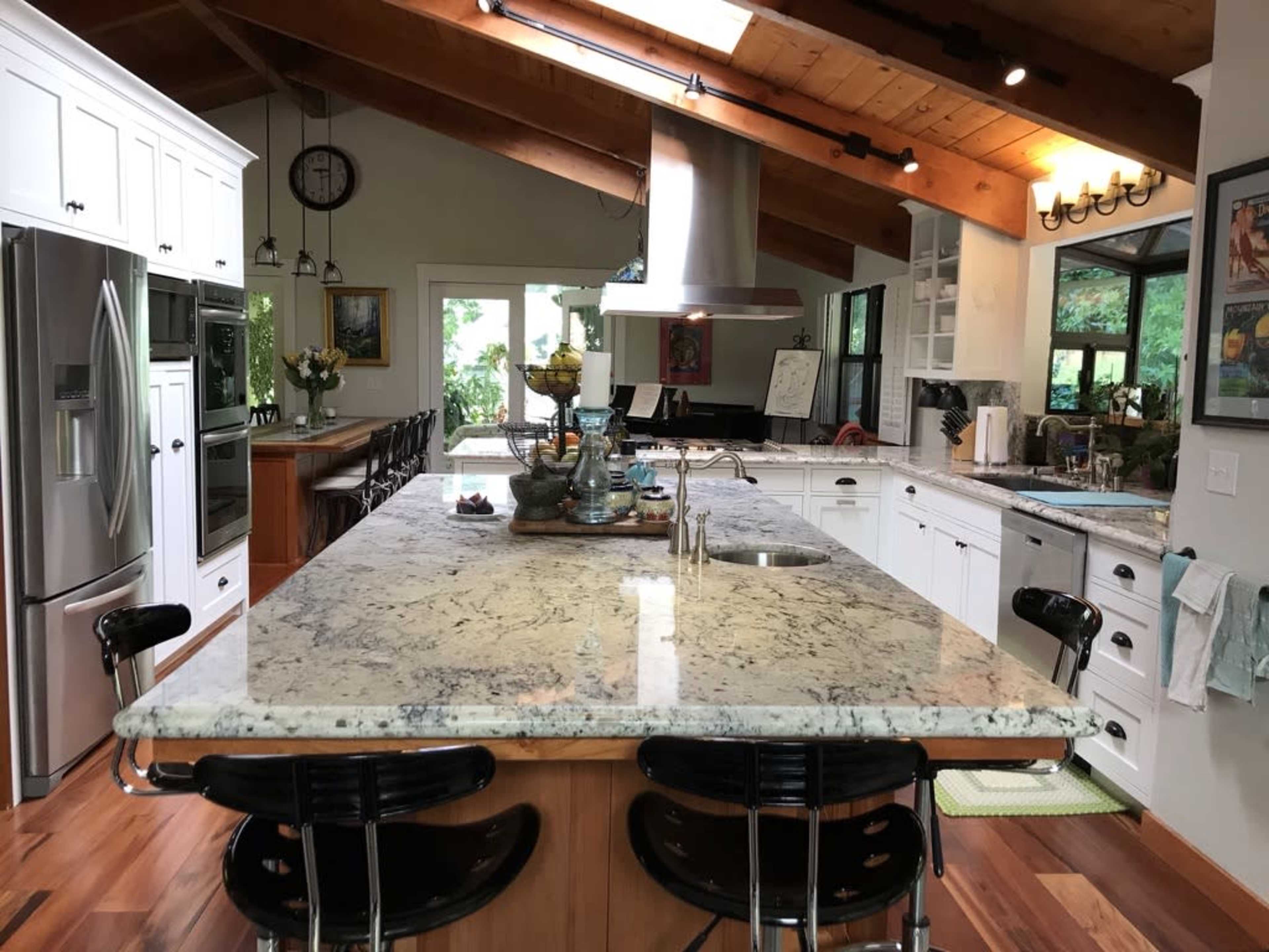 A spacious kitchen features a large granite island, modern appliances, and wooden beams on the ceiling.