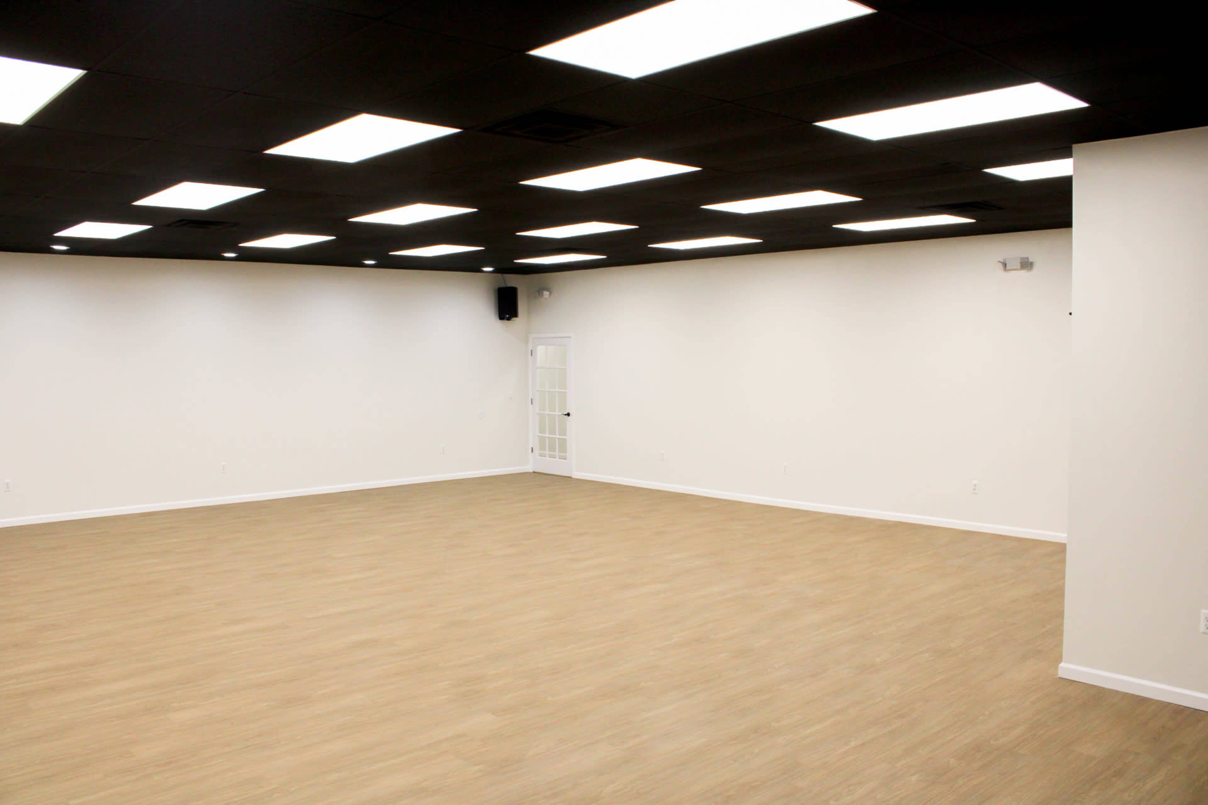 The image shows a spacious, empty room with a light-colored floor and dimmed ceiling lights.