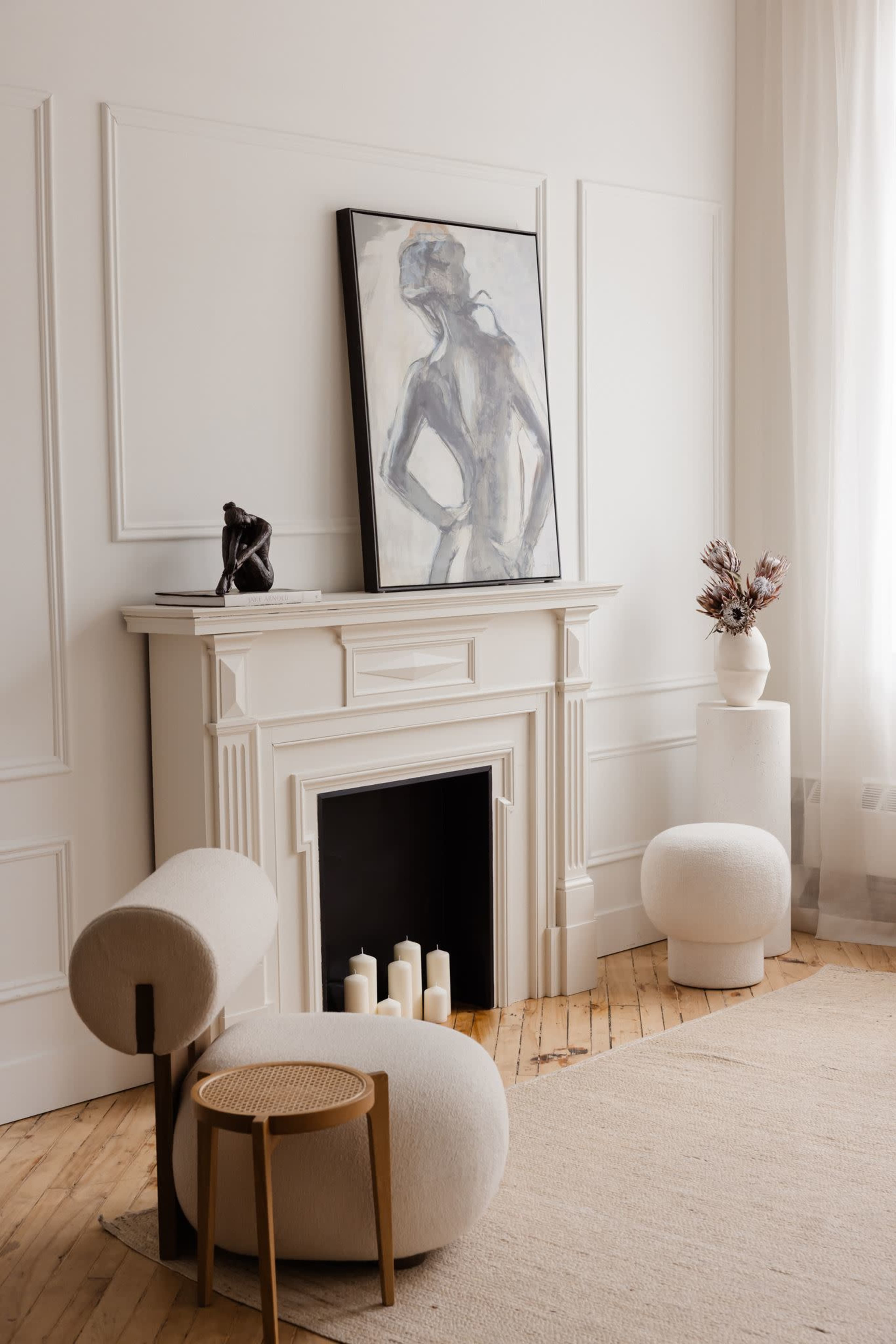 The image shows a minimalist living room with a fireplace, a large artwork on the wall, and modern furniture including sculptural chairs and a small table.