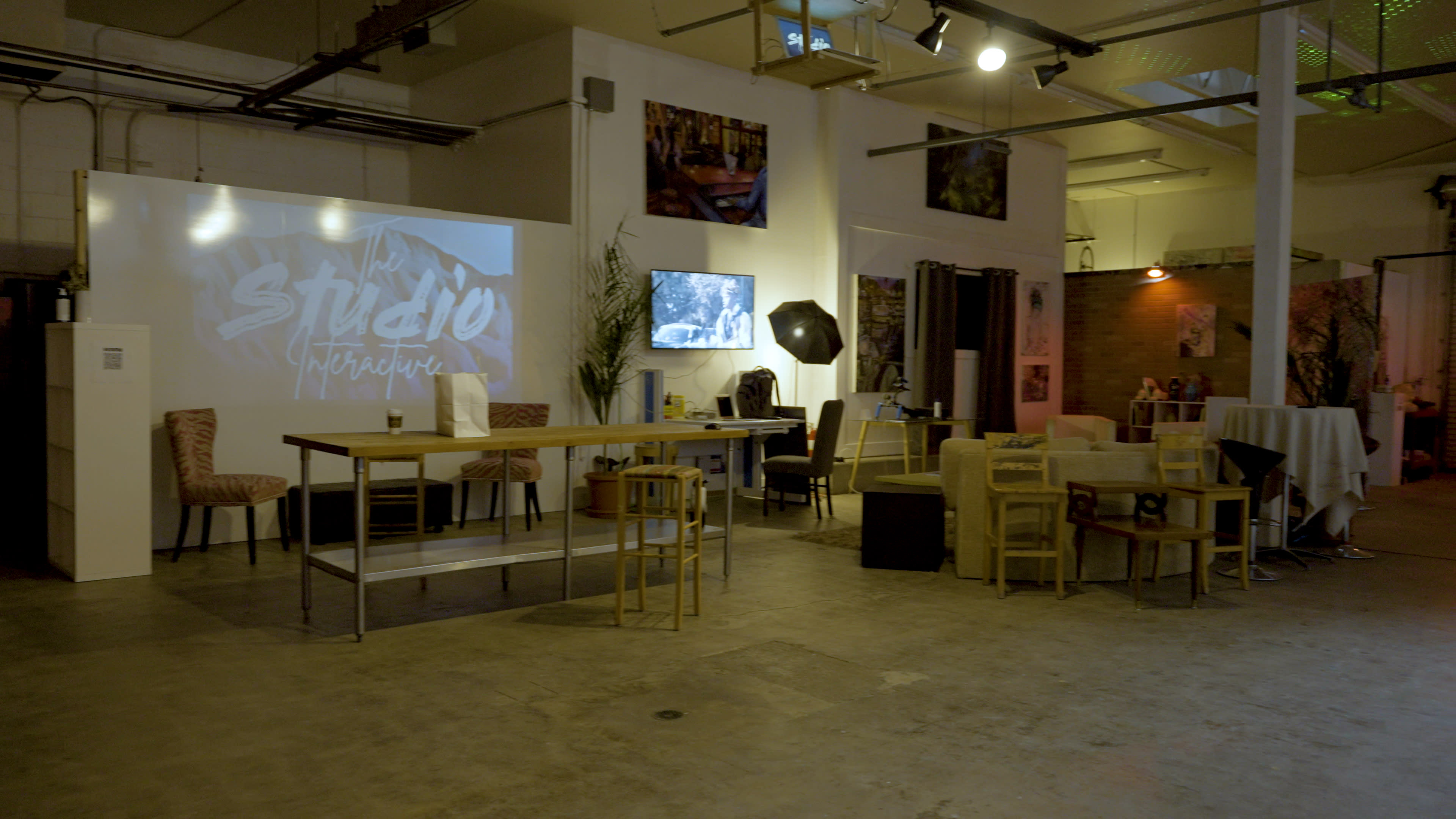 A spacious interior of a studio with various seating arrangements, a large table, and art displayed on the walls.
