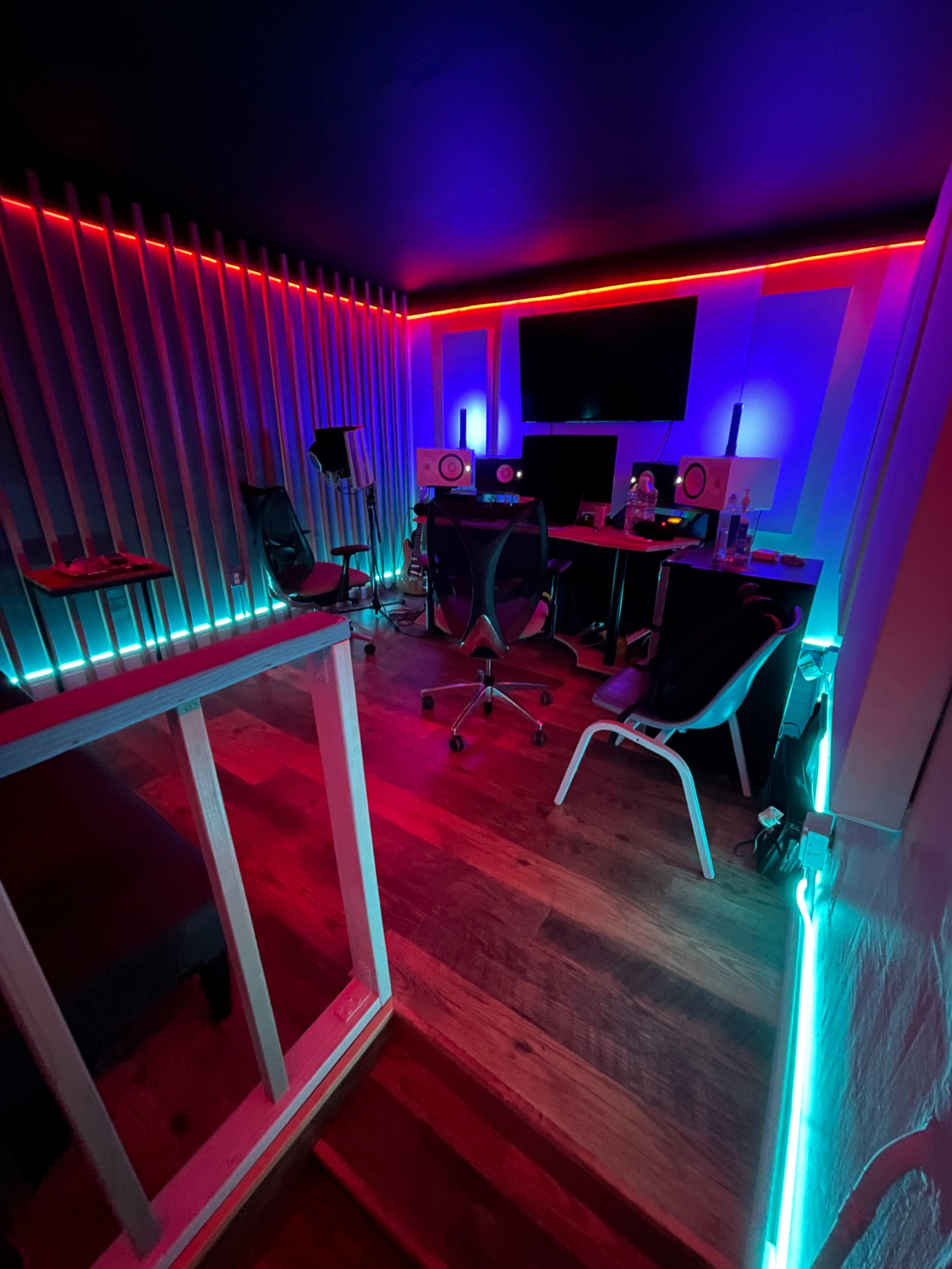 The image shows a music studio with colorful LED lighting, a computer setup, and sound equipment arranged in a modern space.