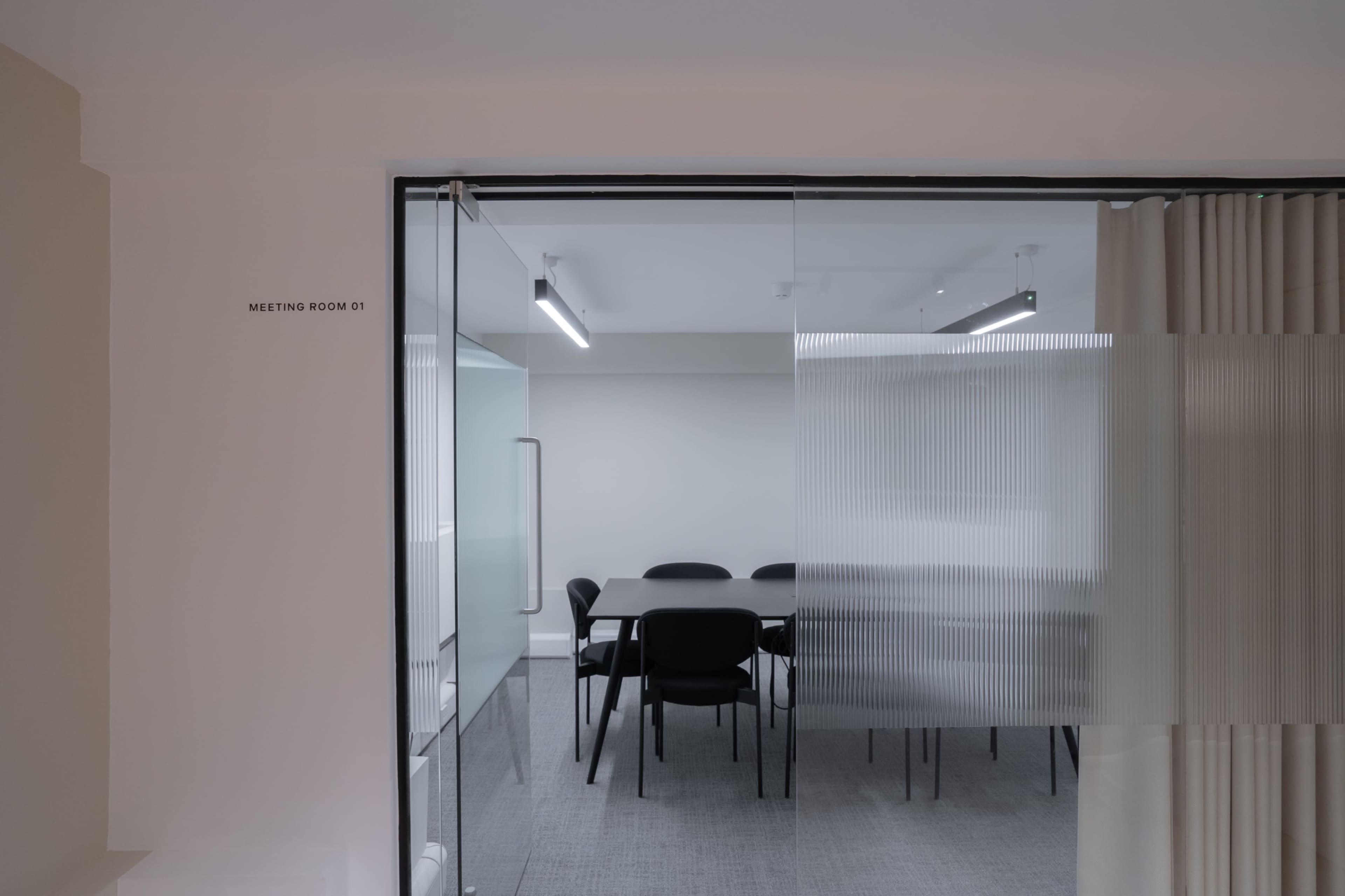 A glass door opens into a modern meeting room with a table and black chairs.