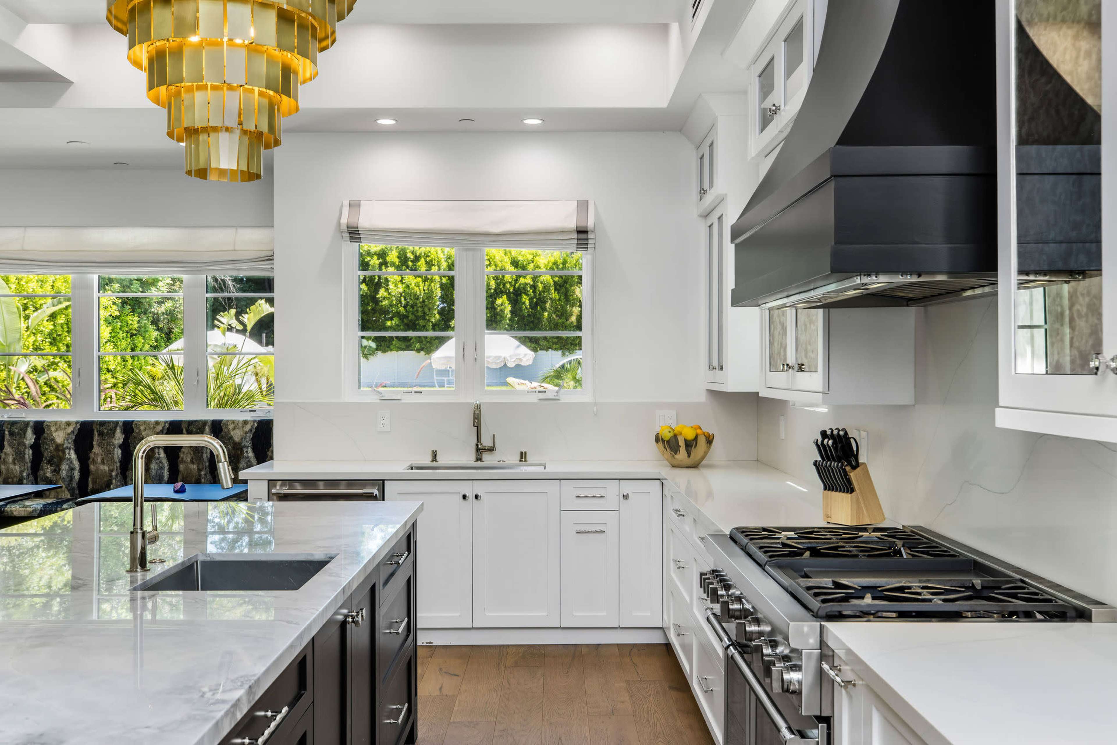 A modern kitchen features white cabinetry, a large marble island, stainless steel appliances, and a decorative golden chandelier.
