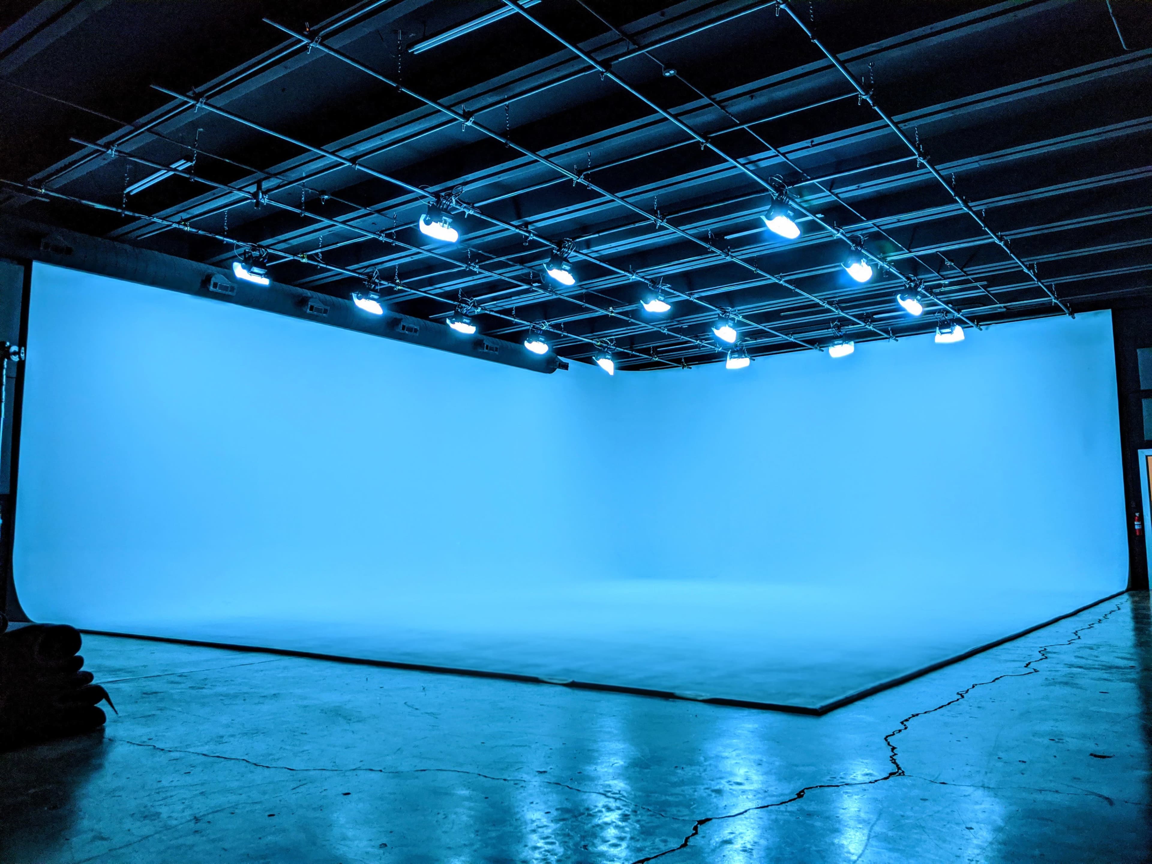 The image shows a spacious photography studio with a large blue backdrop and bright overhead lights illuminating the area.