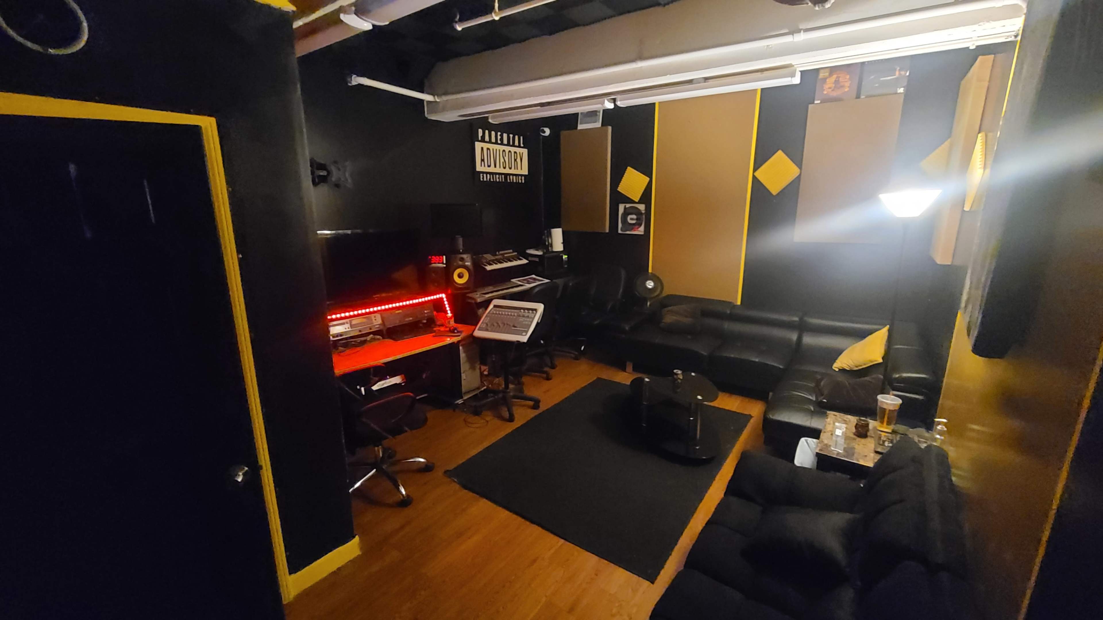 A music studio featuring black and yellow decor, a digital audio workstation setup with equipment, and seating areas.