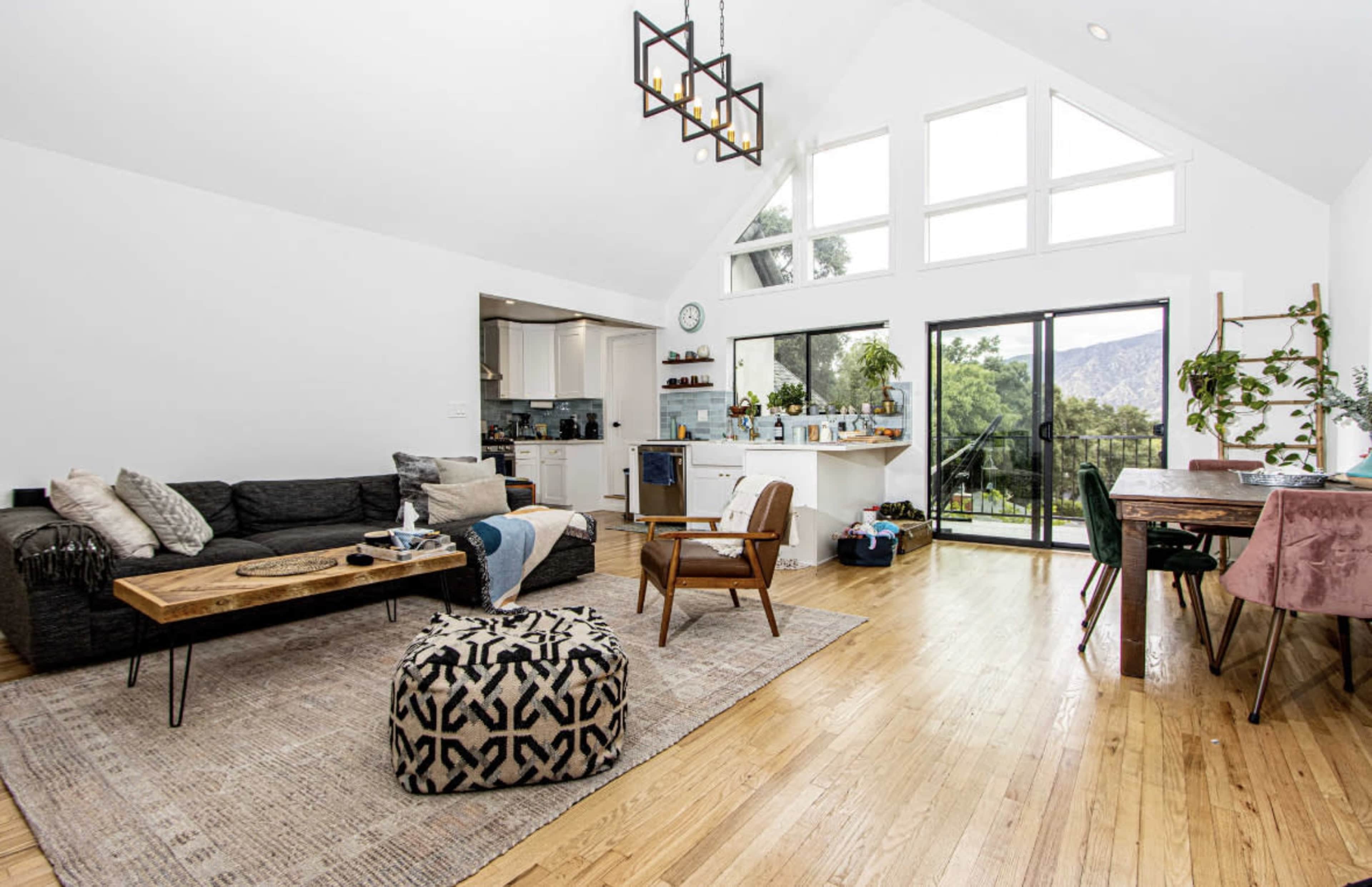 A spacious living area features a black sofa, a wooden coffee table, and large windows overlooking a garden.