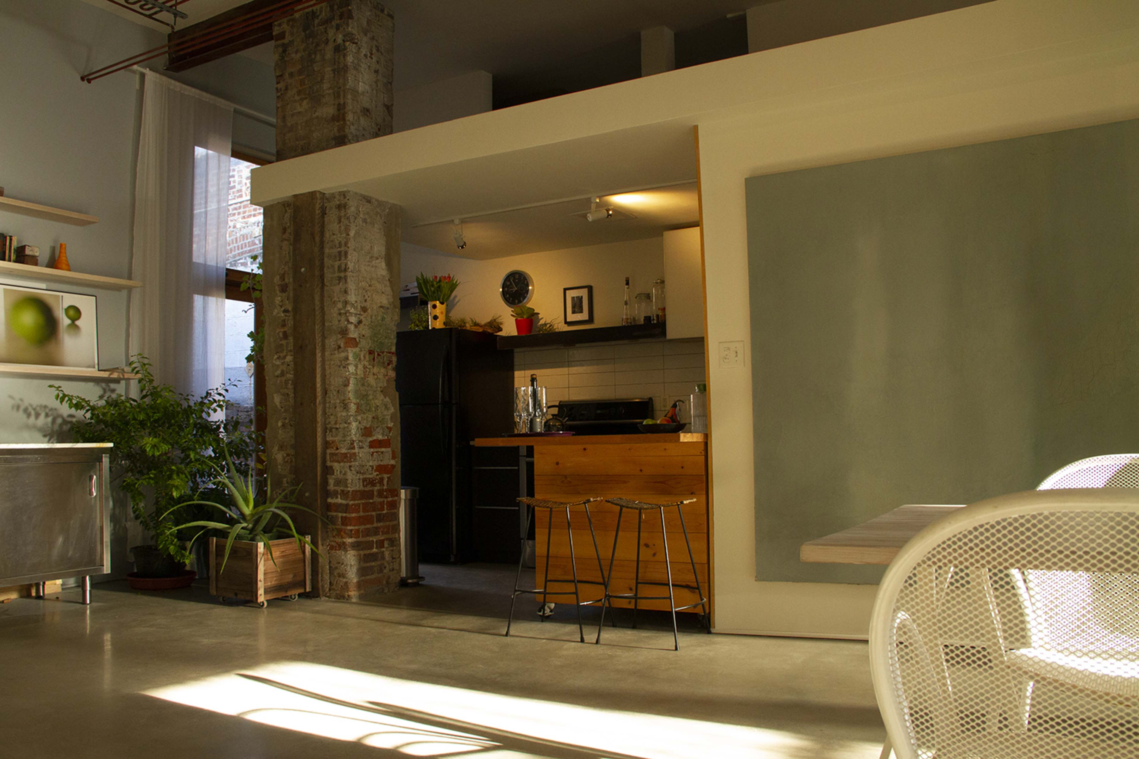 A modern kitchen with a wooden island, black appliances, and a large green wall, all set in an airy, open-concept living space.