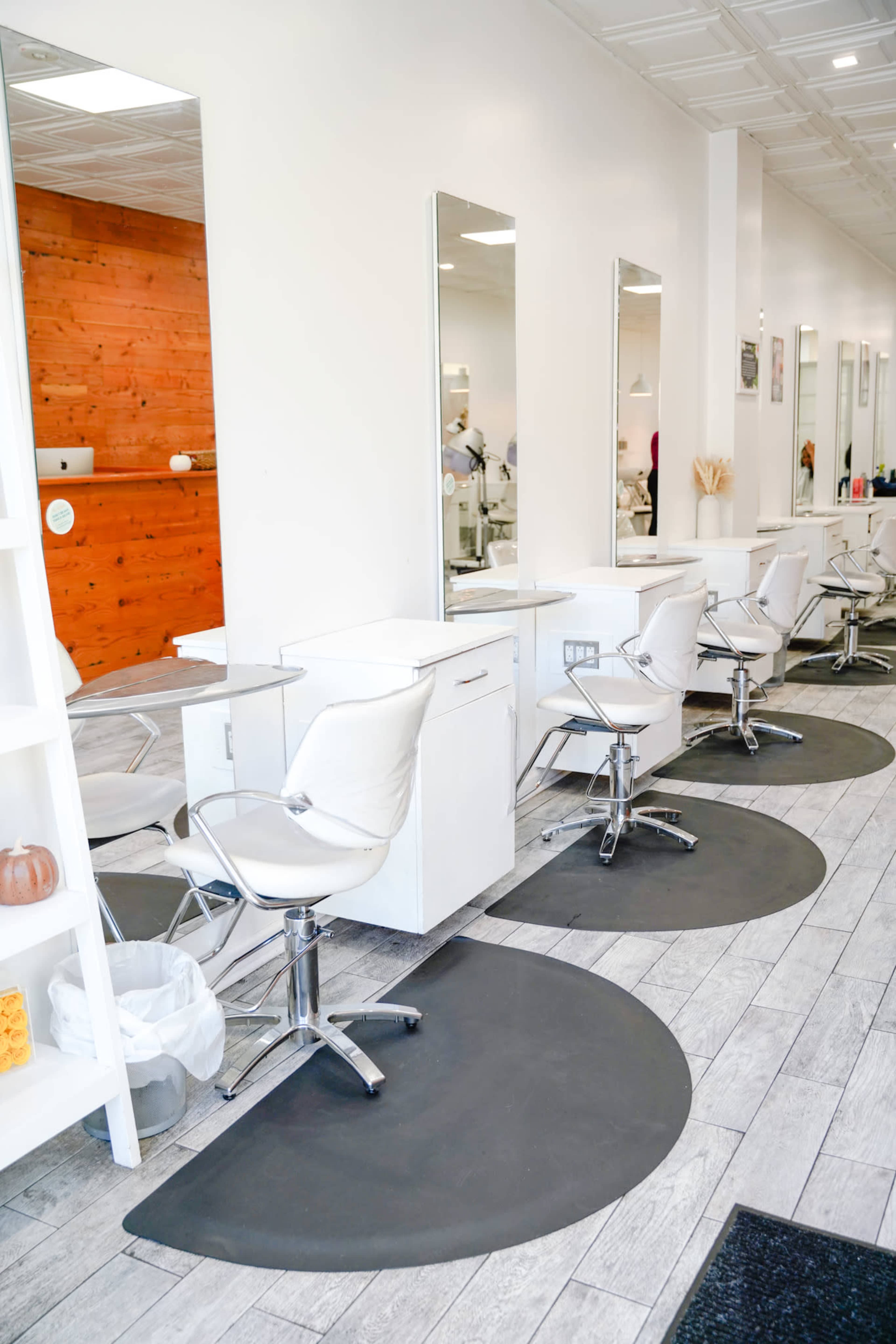 A modern salon interior with several styling stations featuring white chairs and large mirrors along a clean, well-lit wall.