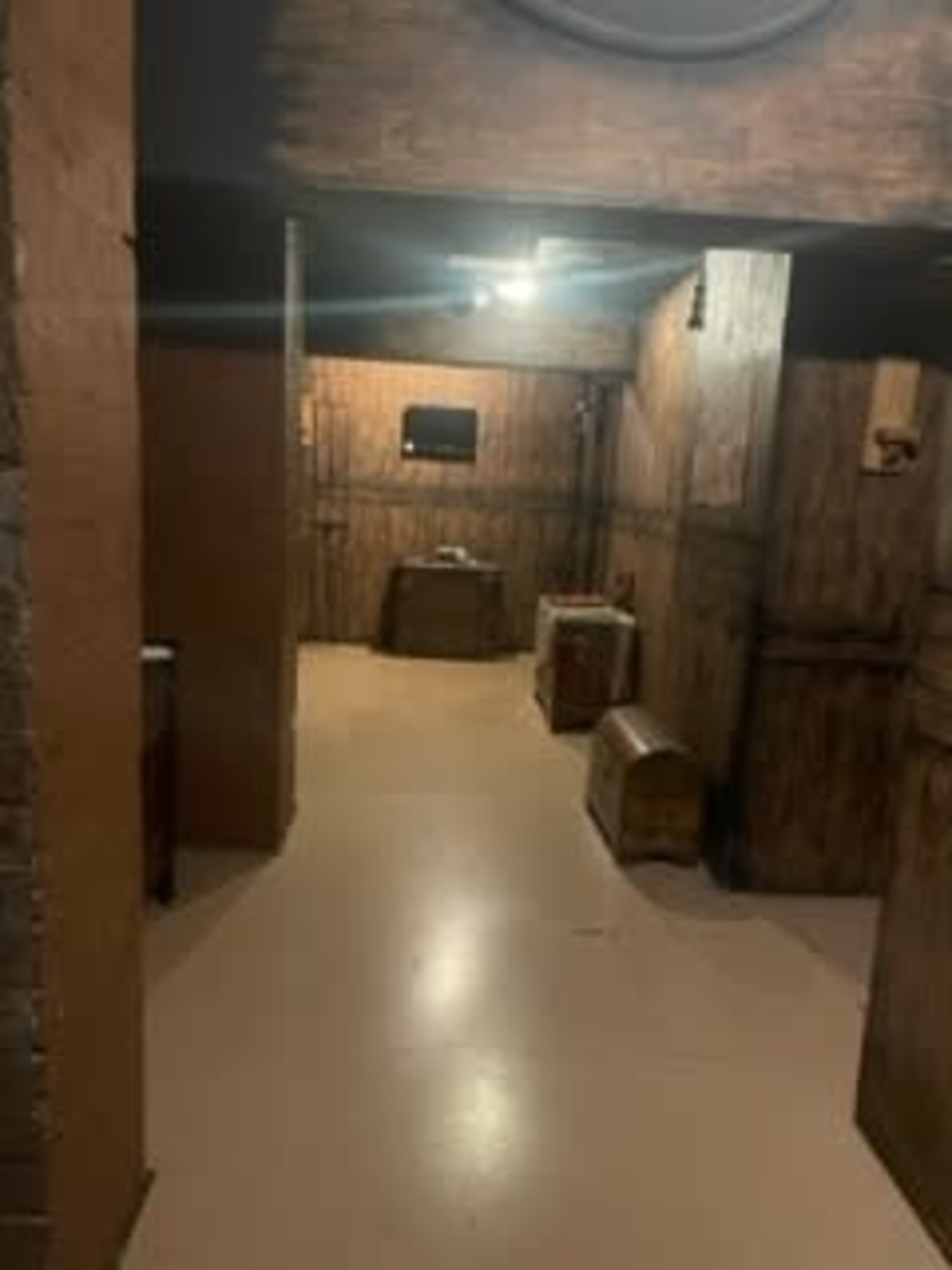 The image shows a dimly lit room with wooden walls, a pale floor, and several brown wooden crates and chests.