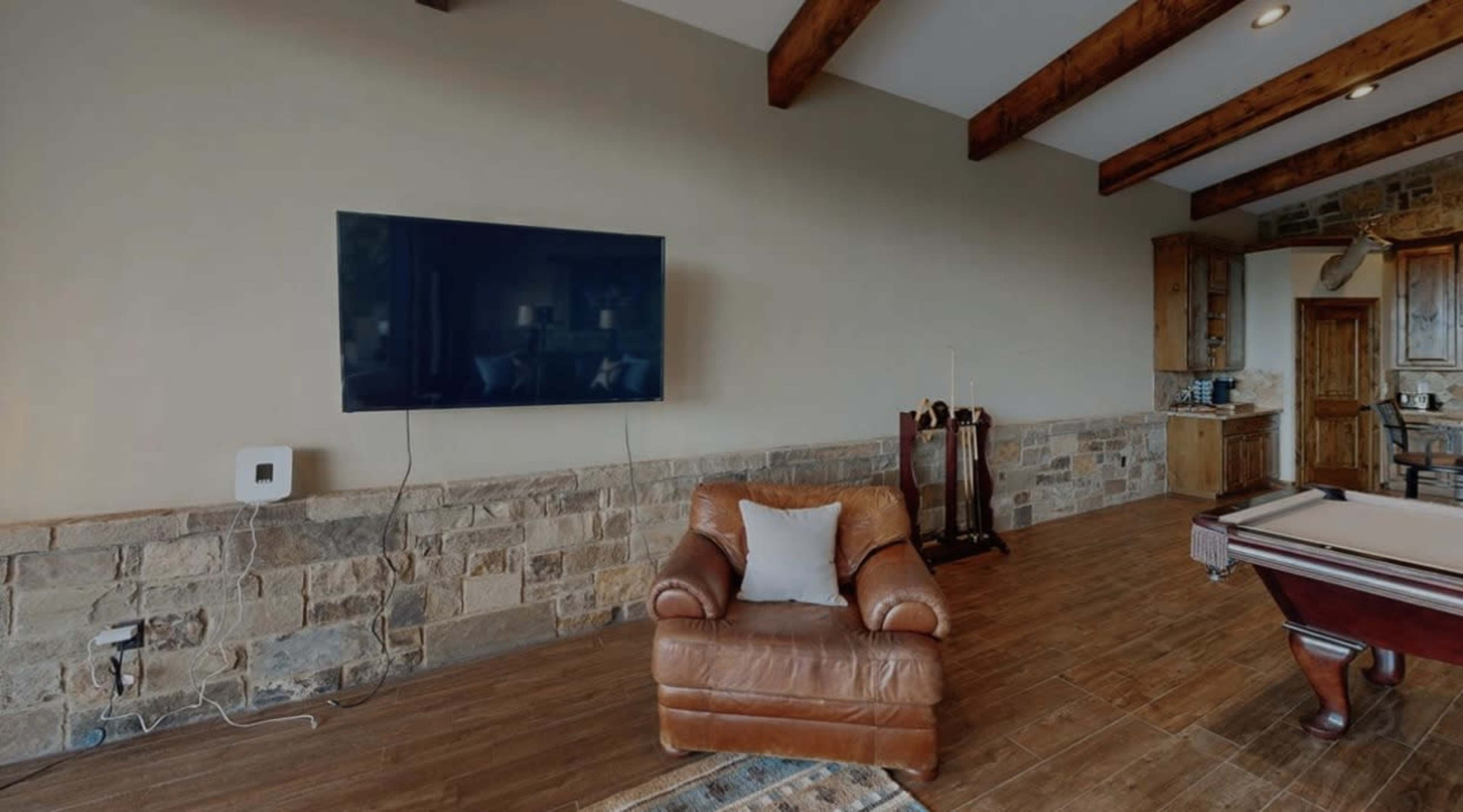 The image shows a room with a leather armchair, a mounted flat-screen TV on a wall, and a stone accent wall.