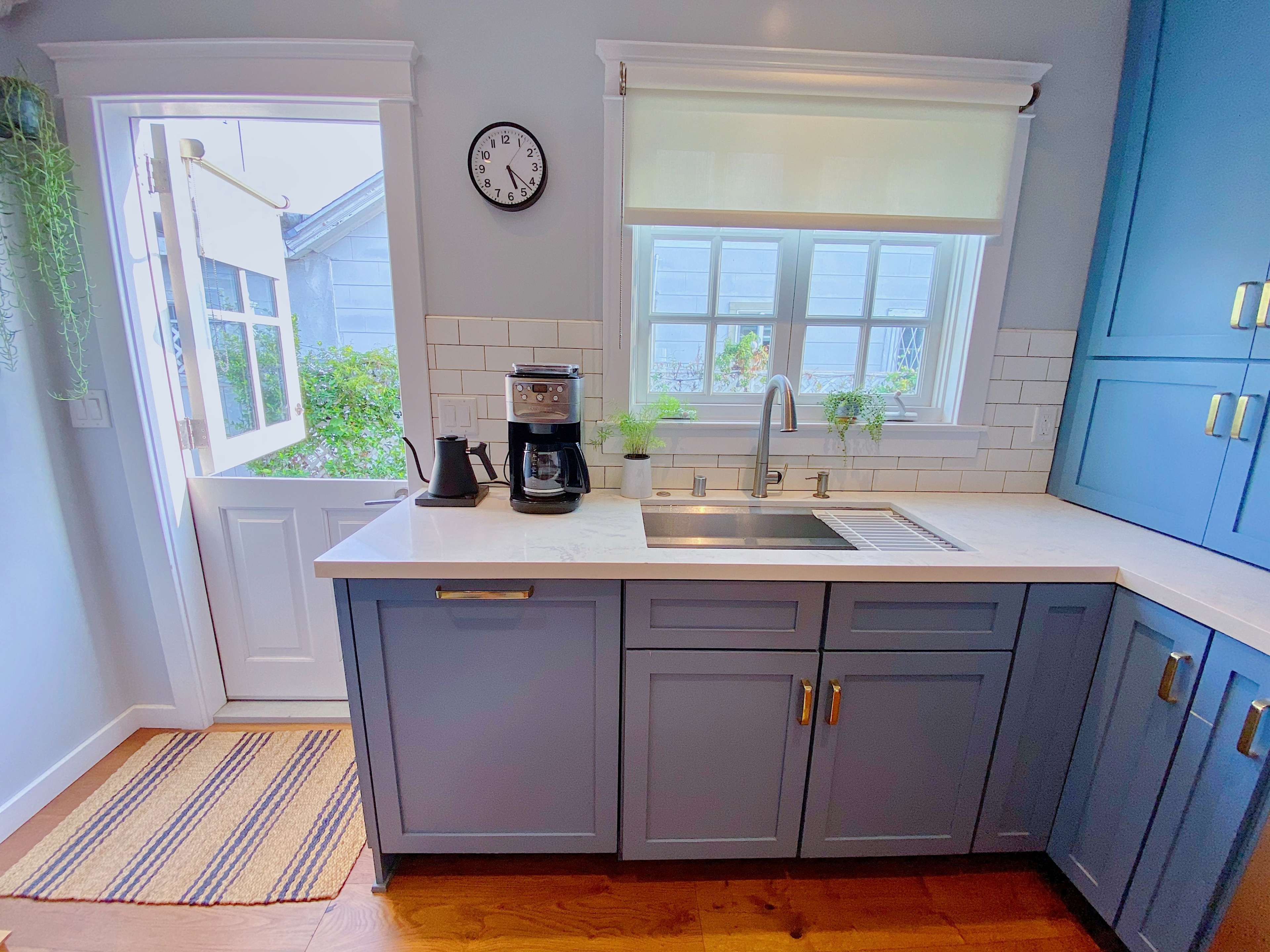A bright kitchen features blue cabinetry, a stainless steel sink, a coffee maker, and a door leading to an outdoor area.