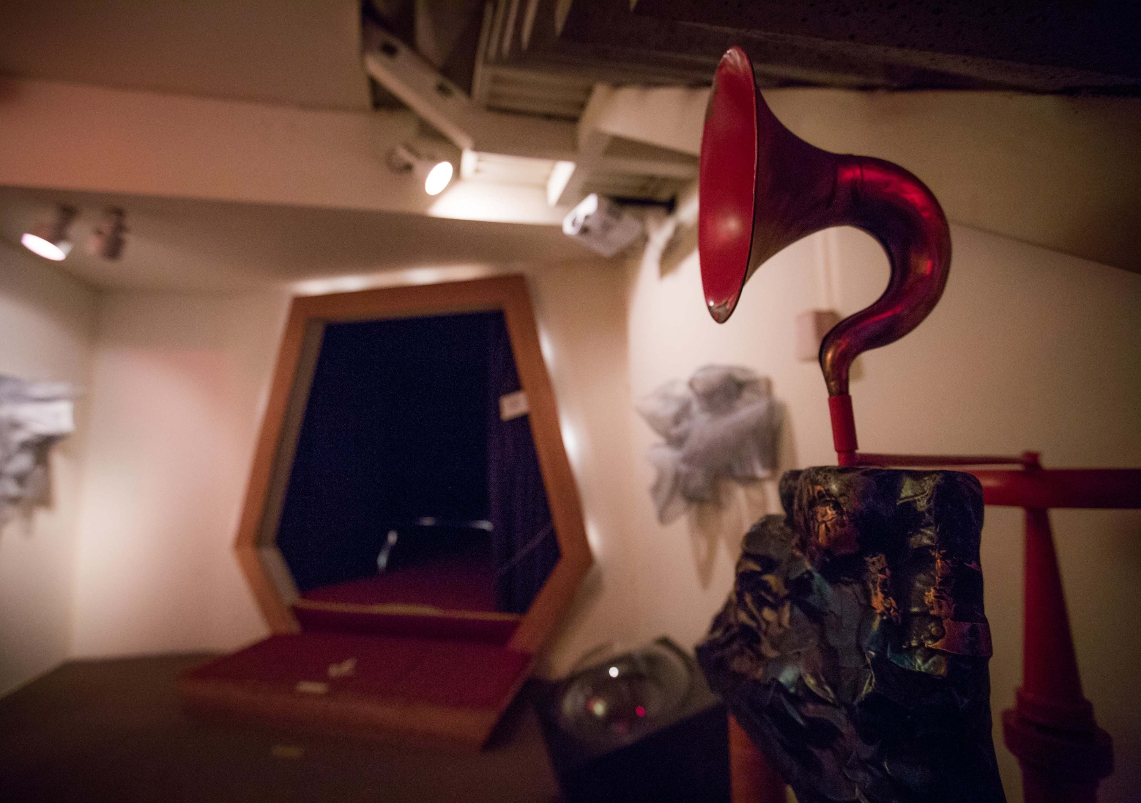 The image shows a red phonograph horn mounted on a metallic base, with a hexagonal doorway in the background leading to a dark space.