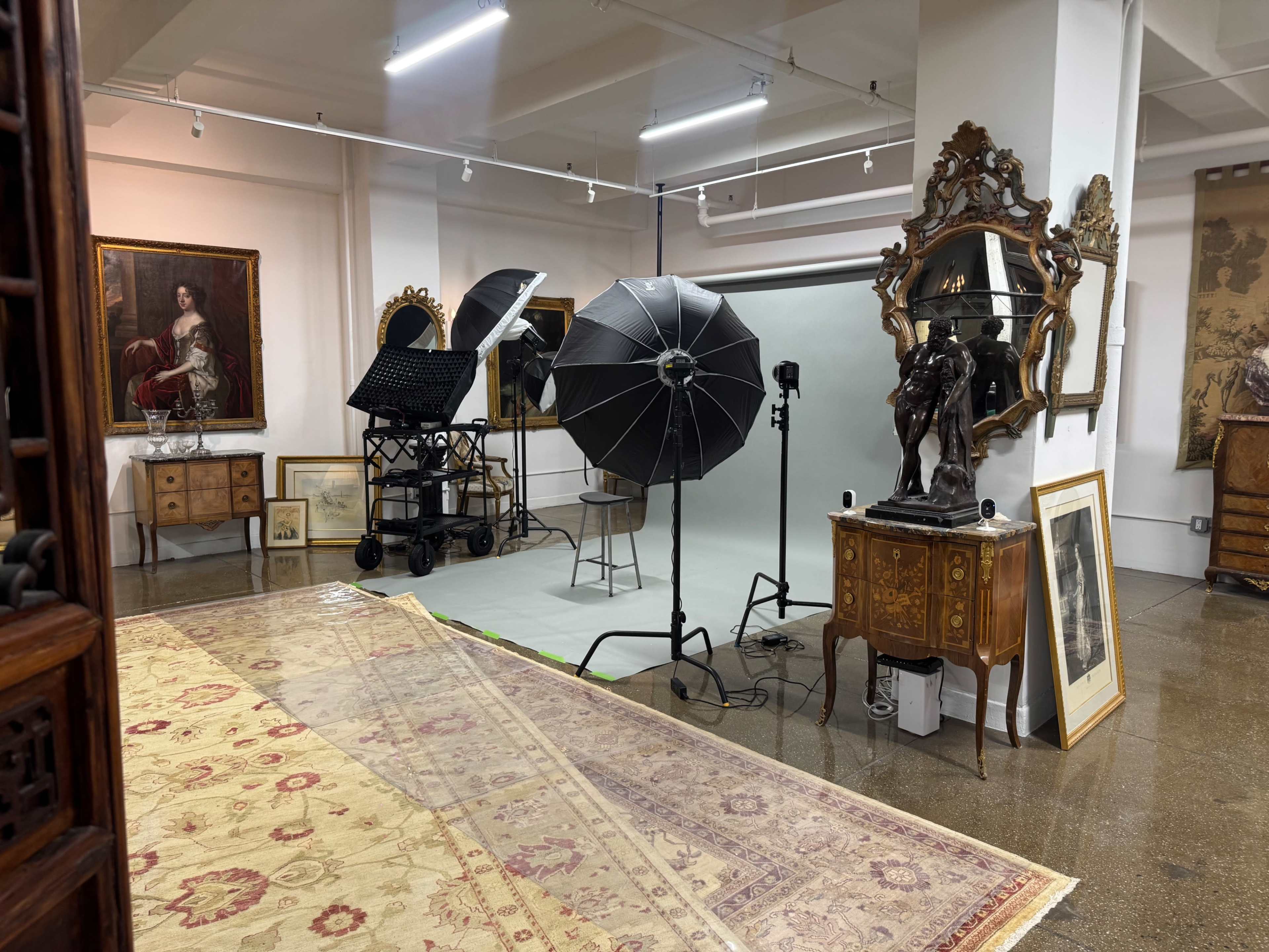 The image shows a photography studio set up with multiple lighting equipment, a backdrop, and various pieces of antique furniture and art along the walls.