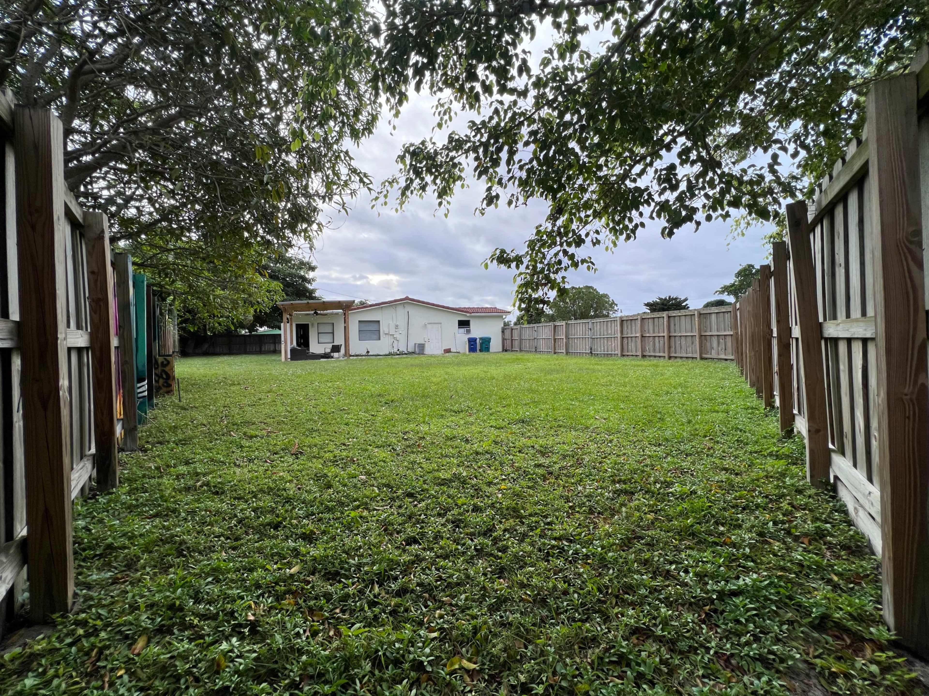 The image shows a spacious, grass-covered yard enclosed by wooden fences, with a single-story house visible in the background.