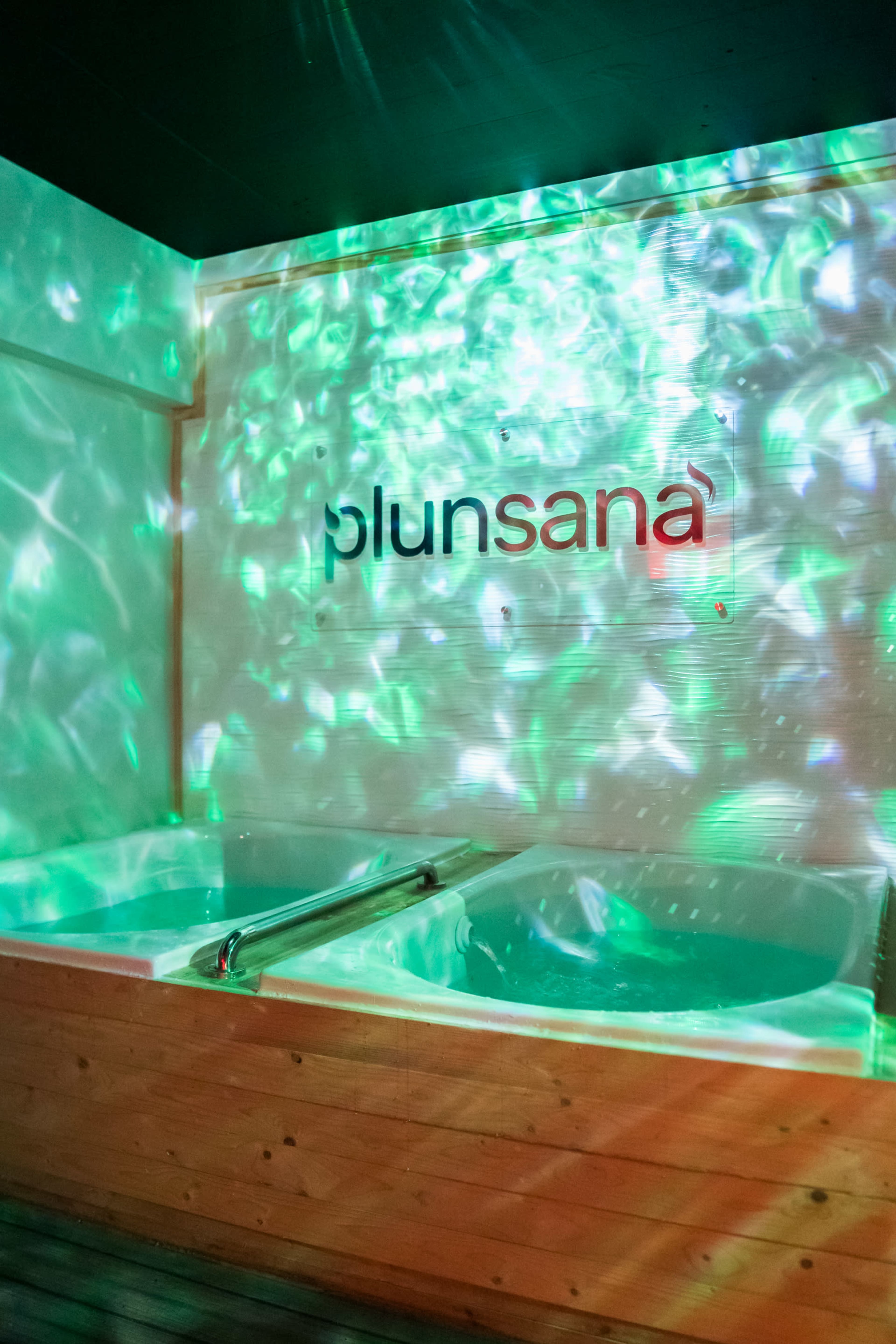 The image shows a spa area featuring two hot tubs with colorful, reflective light patterns projected on the walls.