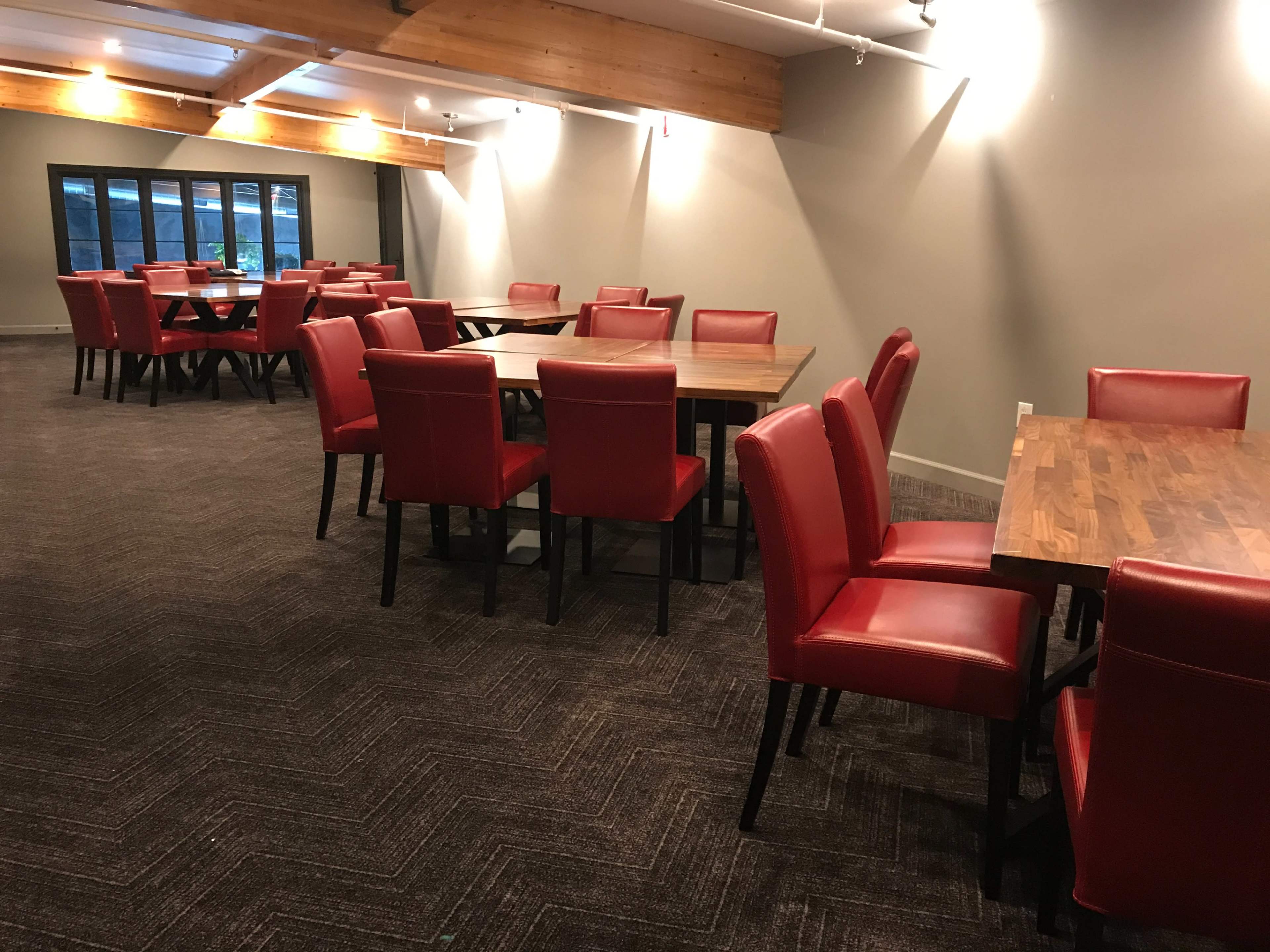A dining area with several wooden tables and red upholstered chairs arranged in rows under wooden beams.