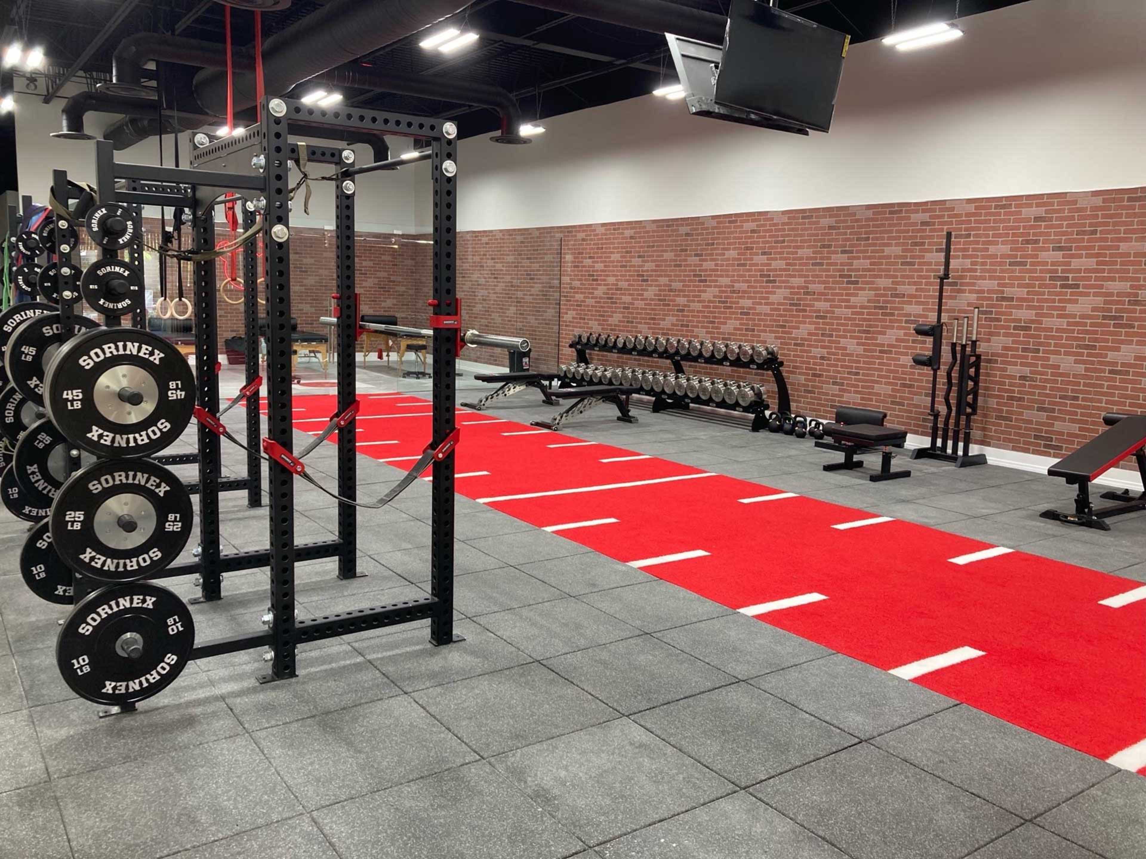 A well-equipped gym featuring weightlifting equipment, a red running track, and a brick wall backdrop.