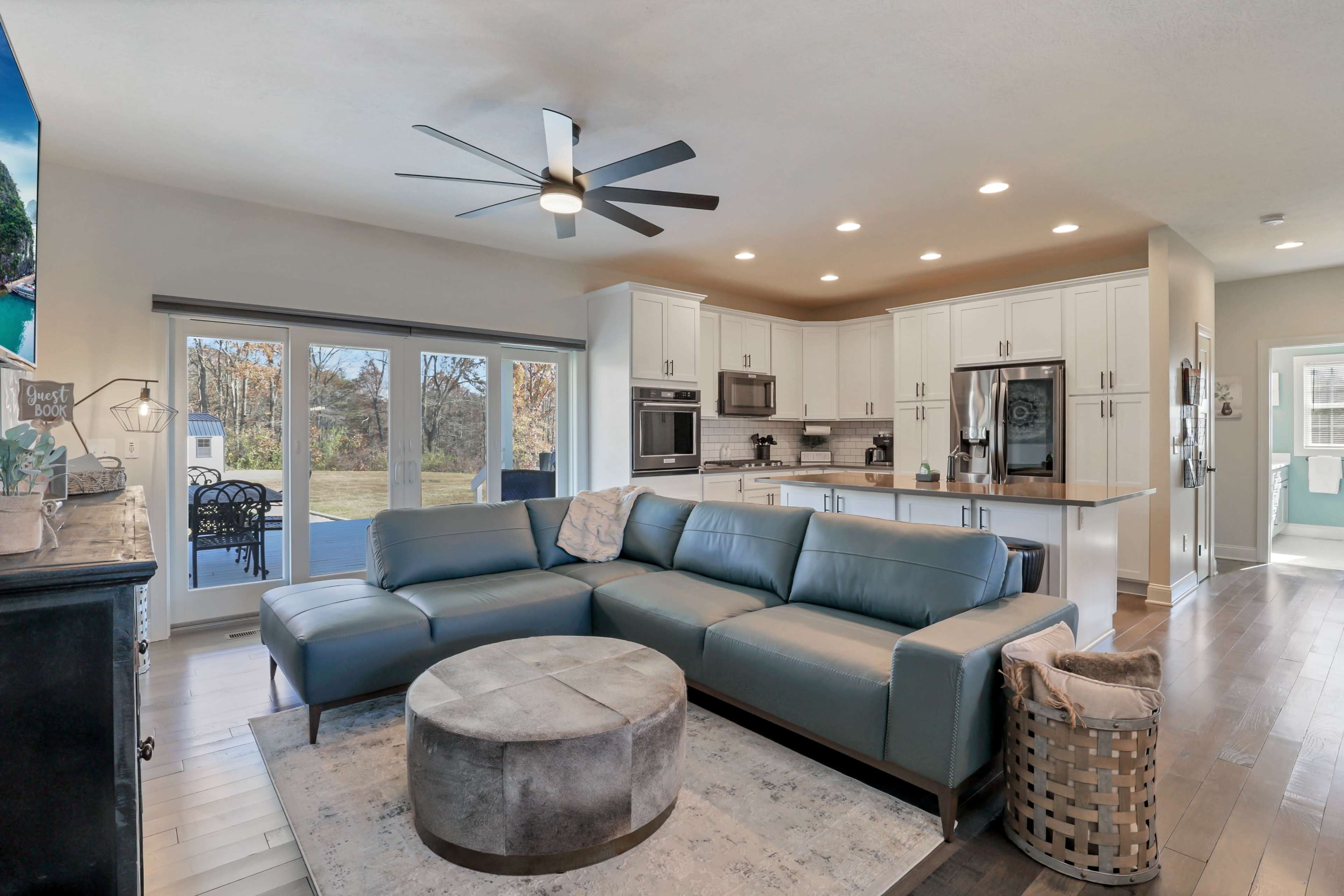A modern living space with a blue sectional sofa, a round coffee table, and an open kitchen featuring white cabinetry and stainless steel appliances.