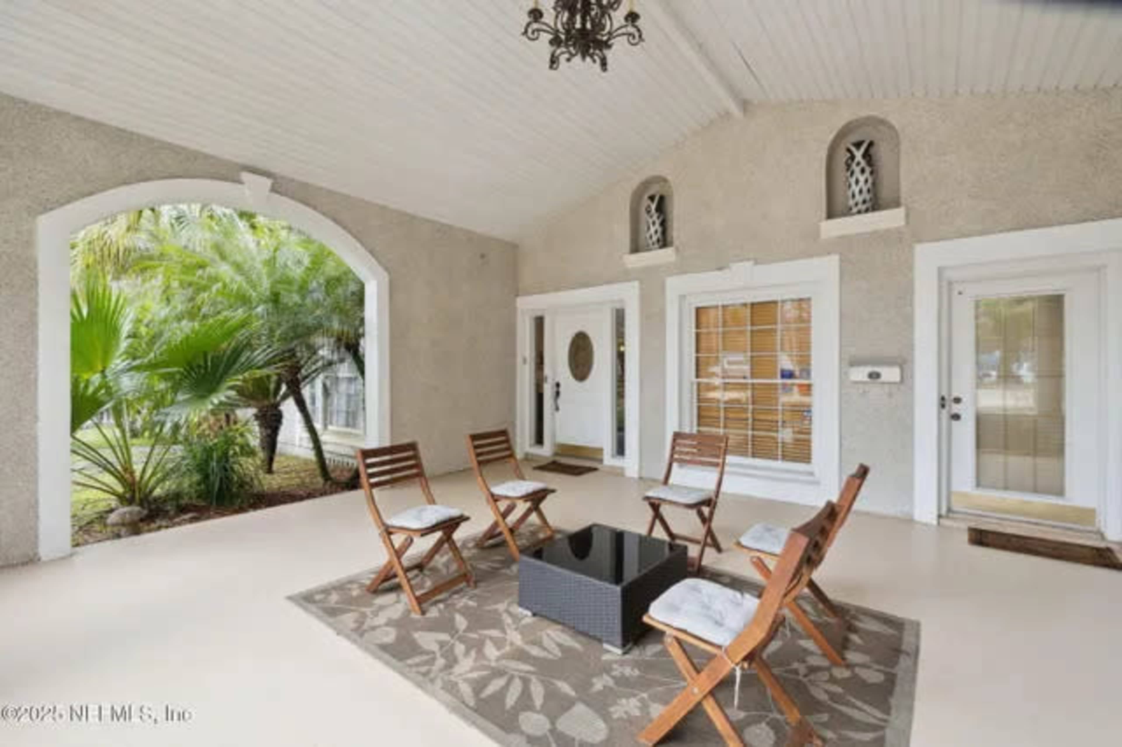 The image shows a covered porch area furnished with six wooden chairs arranged around a small table on a patterned rug.