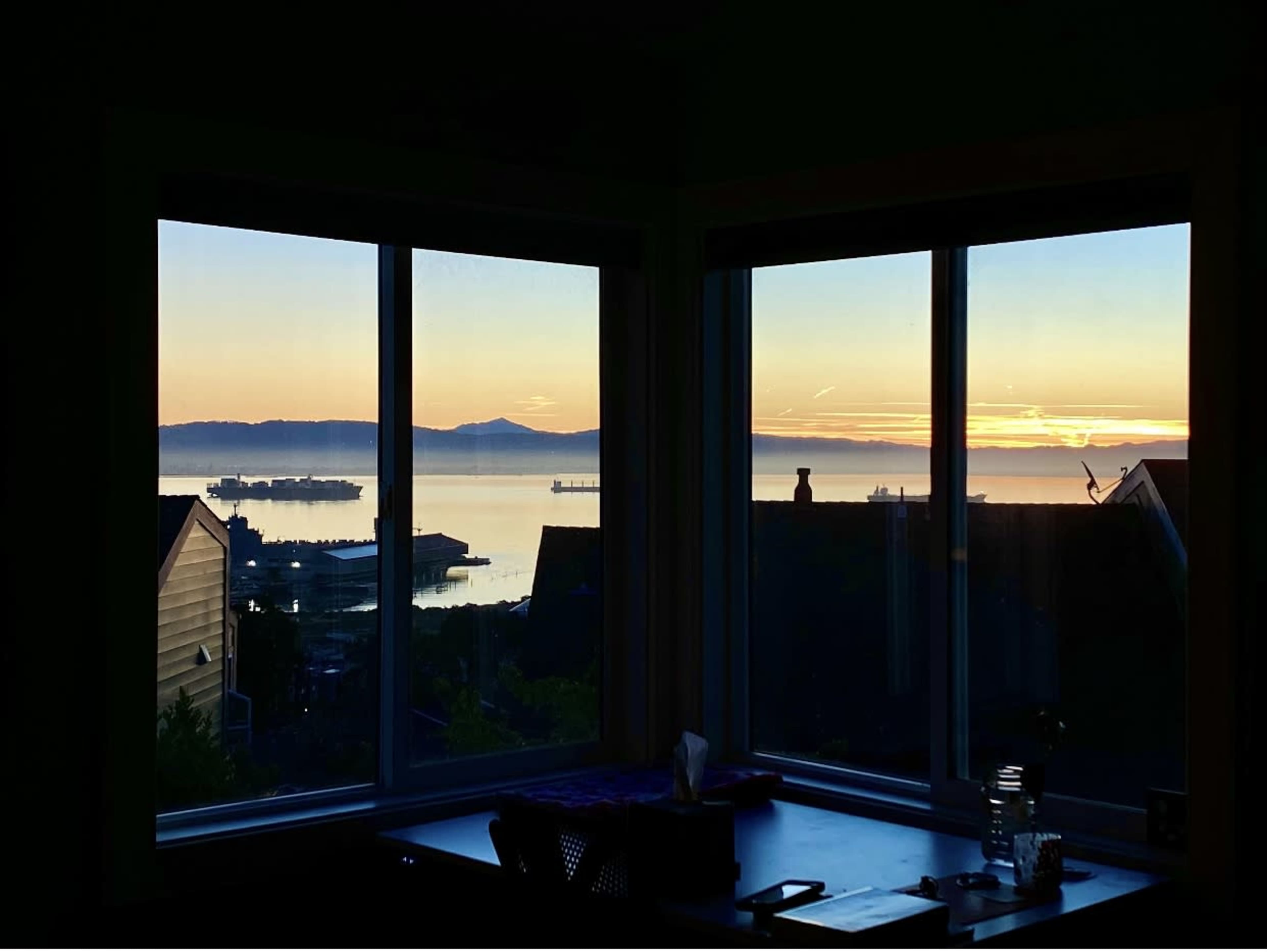 A panoramic view of a sunset over a bay, framed by a set of large windows.
