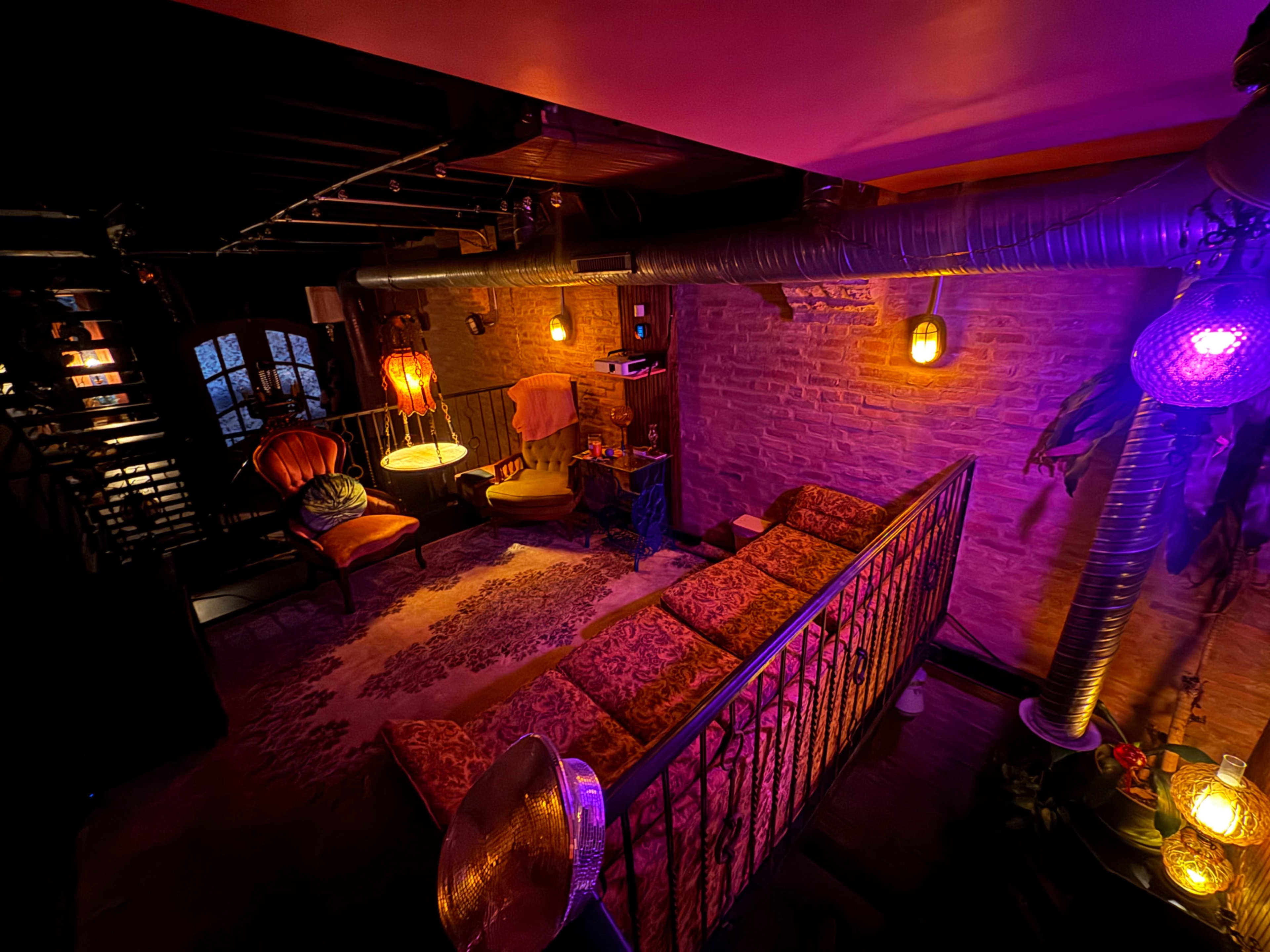 The image shows a dimly lit room with a vintage-style sofa, a small table, and decorative lighting, creating an intimate atmosphere.