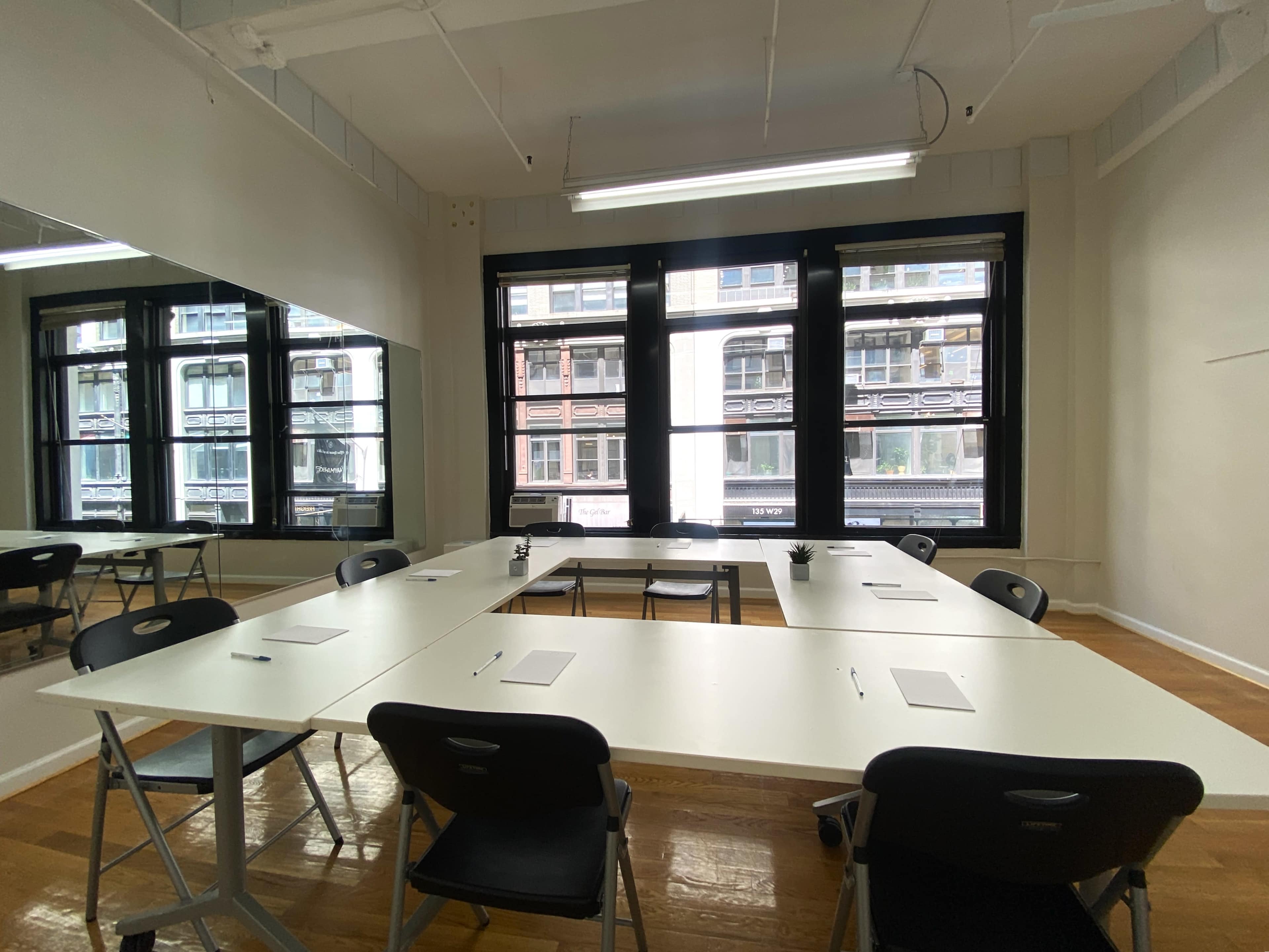 A conference room features a large rectangular table surrounded by black chairs, with several notepads placed on the table and large windows providing natural light.
