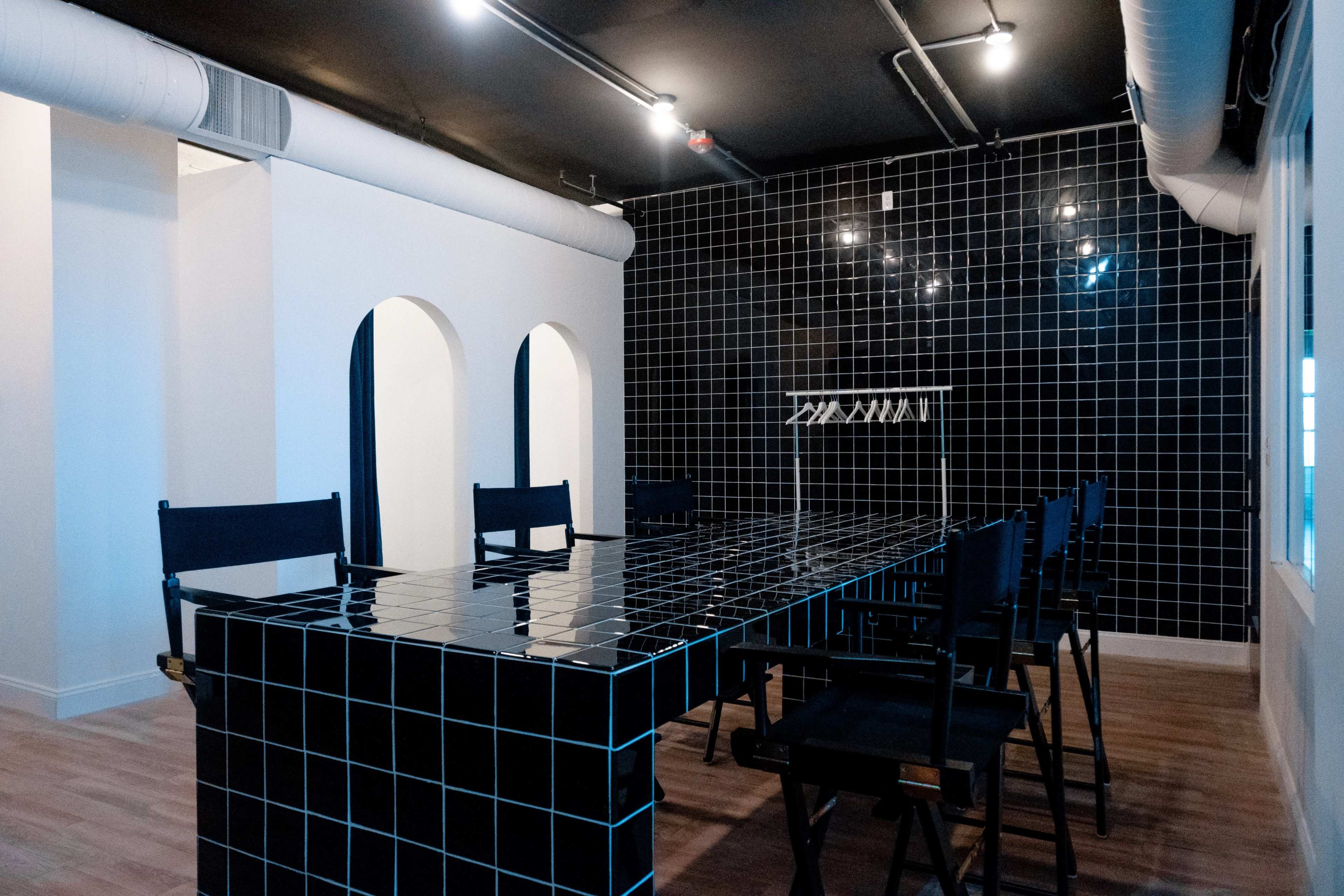 A modern meeting room featuring a large black tiled table surrounded by black chairs, with a black tiled wall and arched openings on one side.