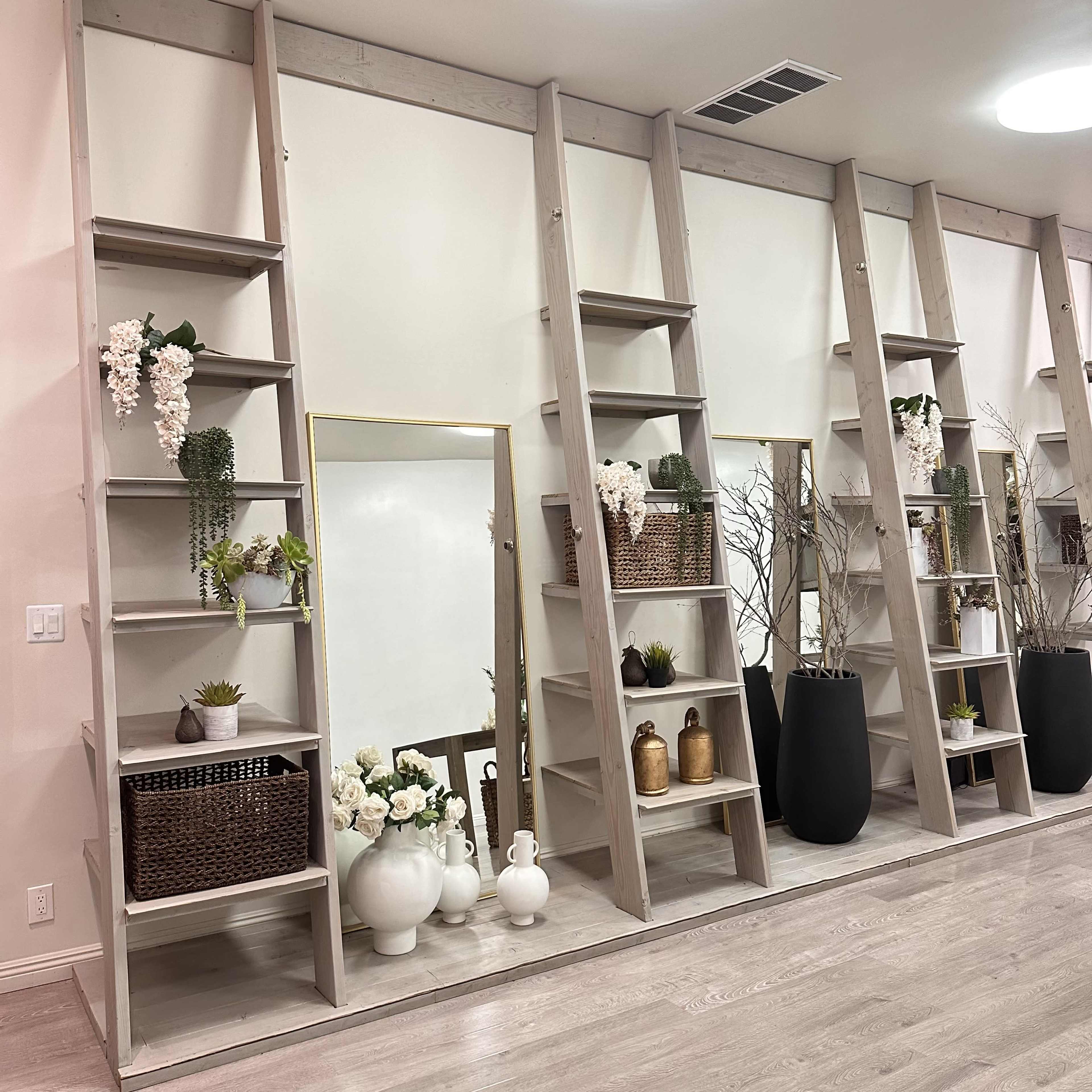 A contemporary interior space featuring a wall with wooden shelving units, adorned with plants, vases, and decorative baskets, alongside a large mirror.