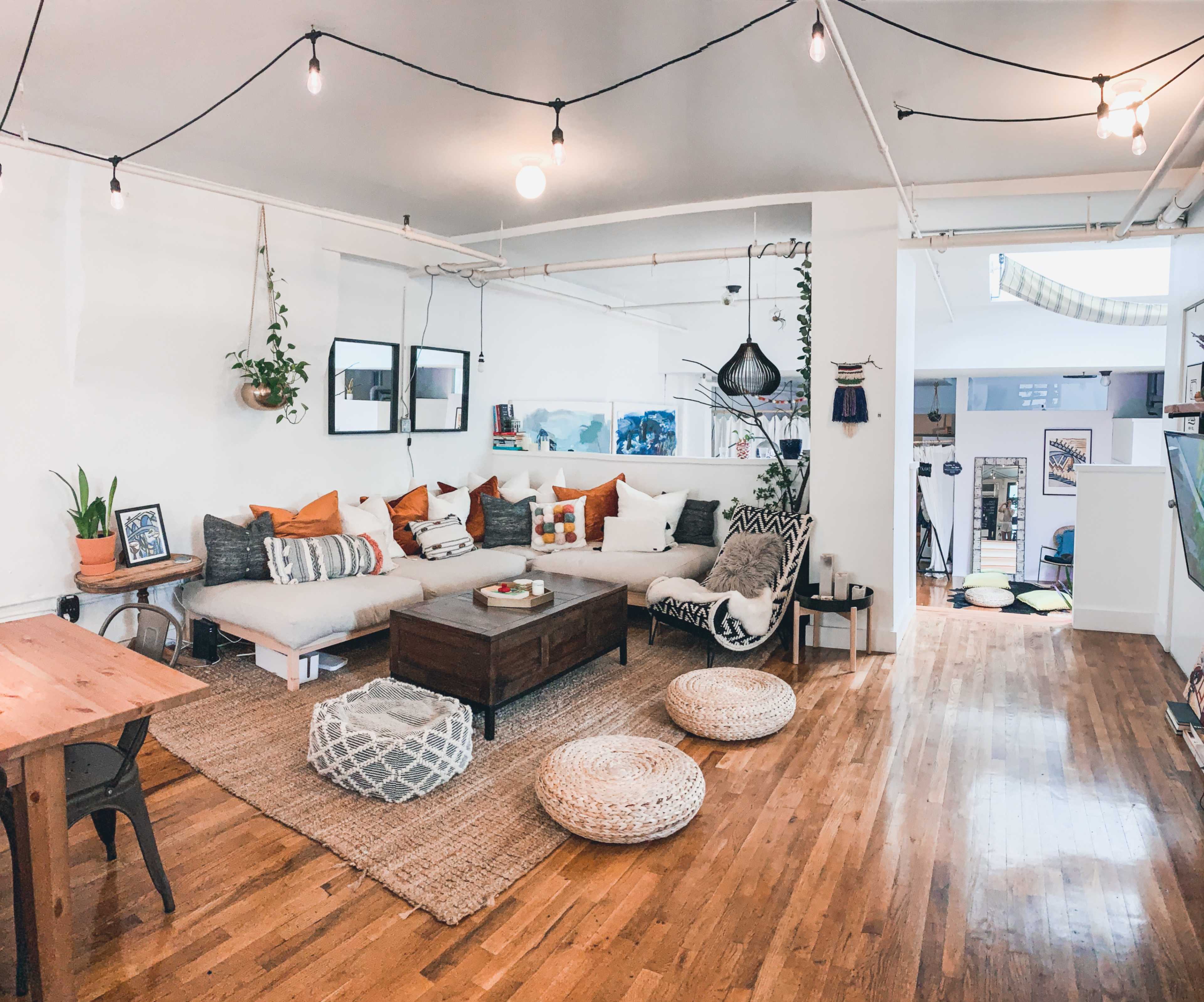 A modern living room features a large sectional sofa, a wooden coffee table, and various decorative pillows, with a dining area visible in the background.